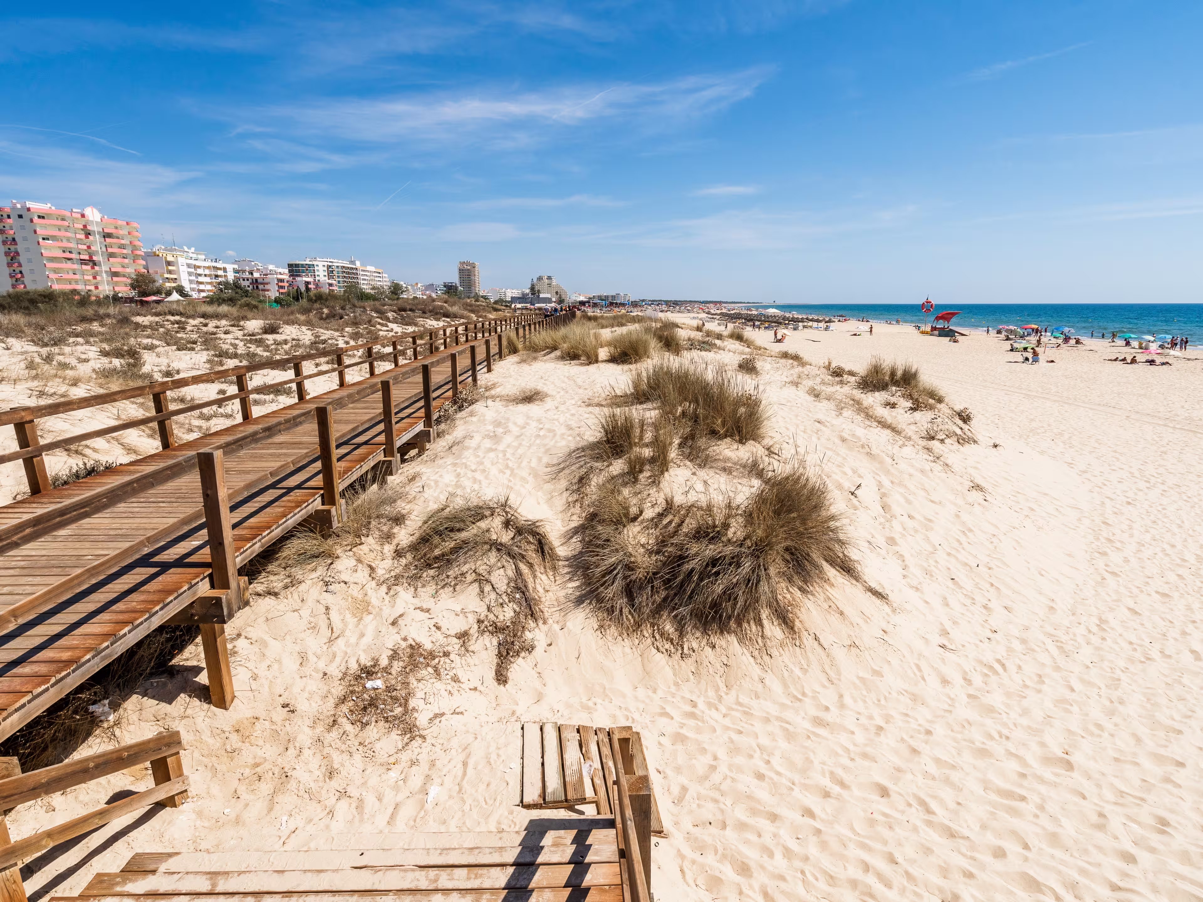 Wide sandy beach with wooden bridges along the dunes in Monte Gordo, Algarve, Portugal