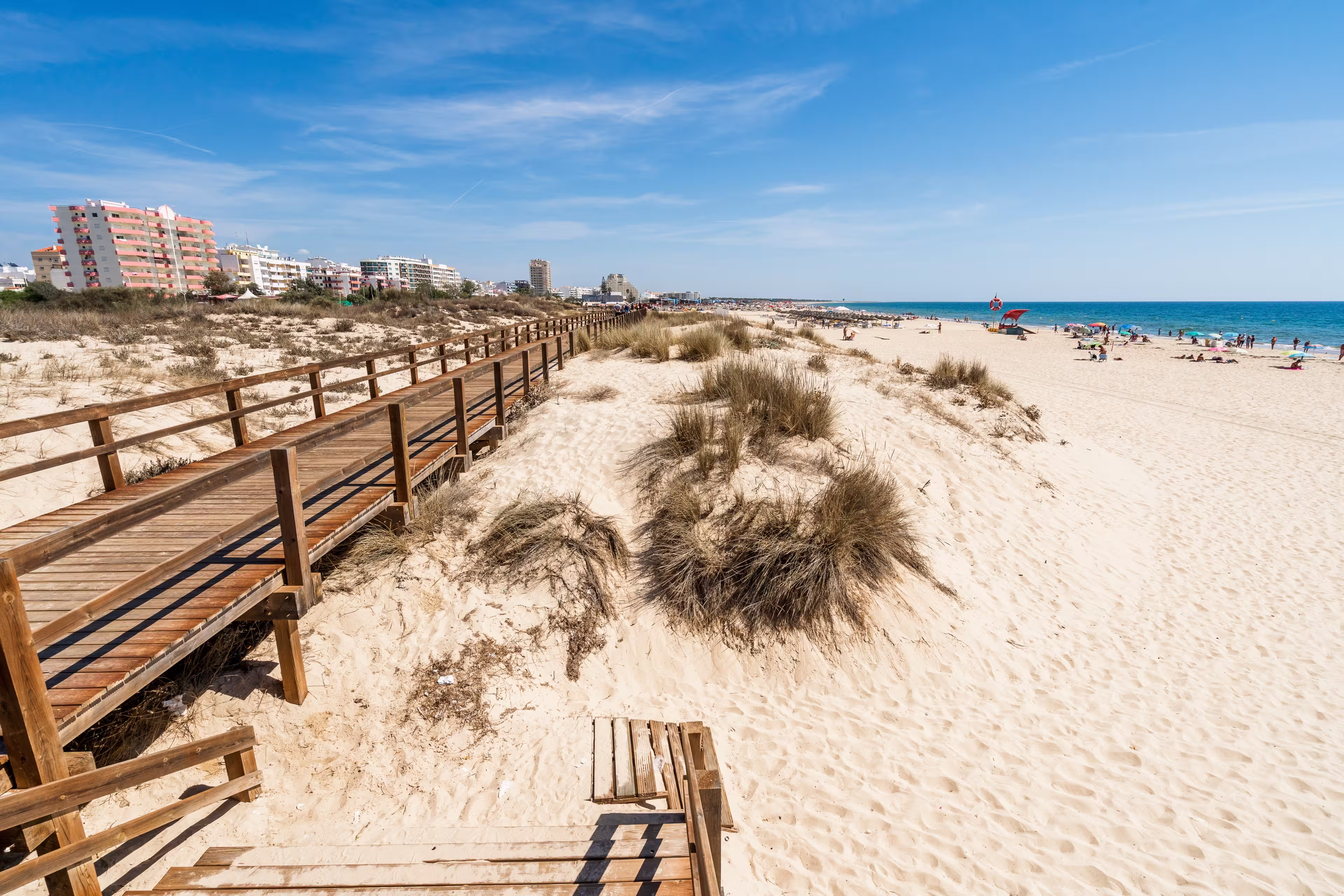 Wide sandy beach with wooden bridges along the dunes in Monte Gordo, Algarve, Portugal