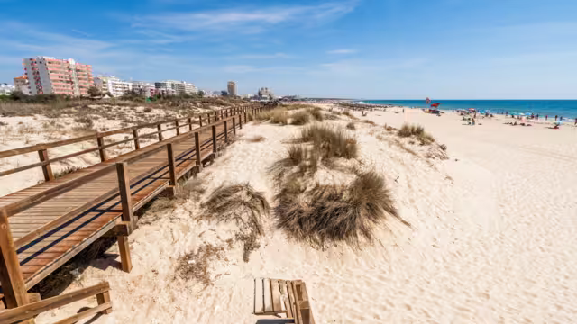 Wide sandy beach with wooden bridges along the dunes in Monte Gordo, Algarve, Portugal