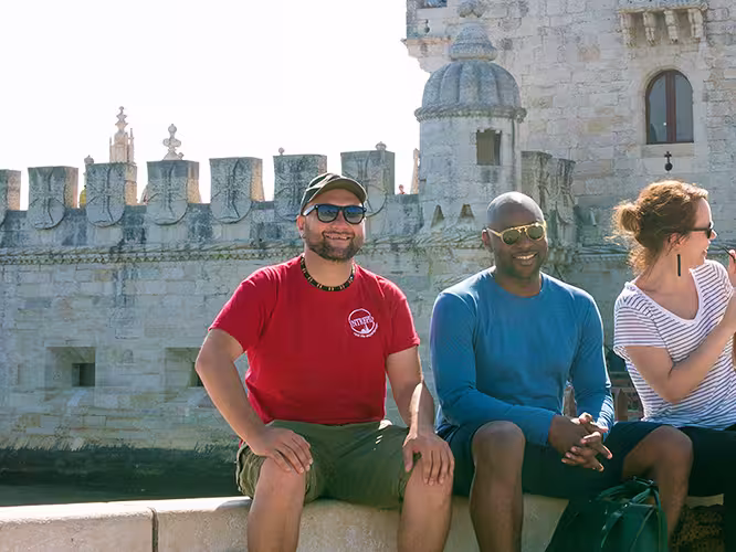 Intrepid Travel group sitting on river bank in front of Belem Tower, Lisbon, Portugal