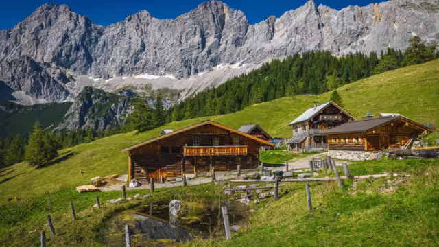 Admirable alpine landscape, wooden log houses on the slope and picturesque high mountains in background, Dachstein mountain group, Ramsau am Dachstein, Austria, Europe
