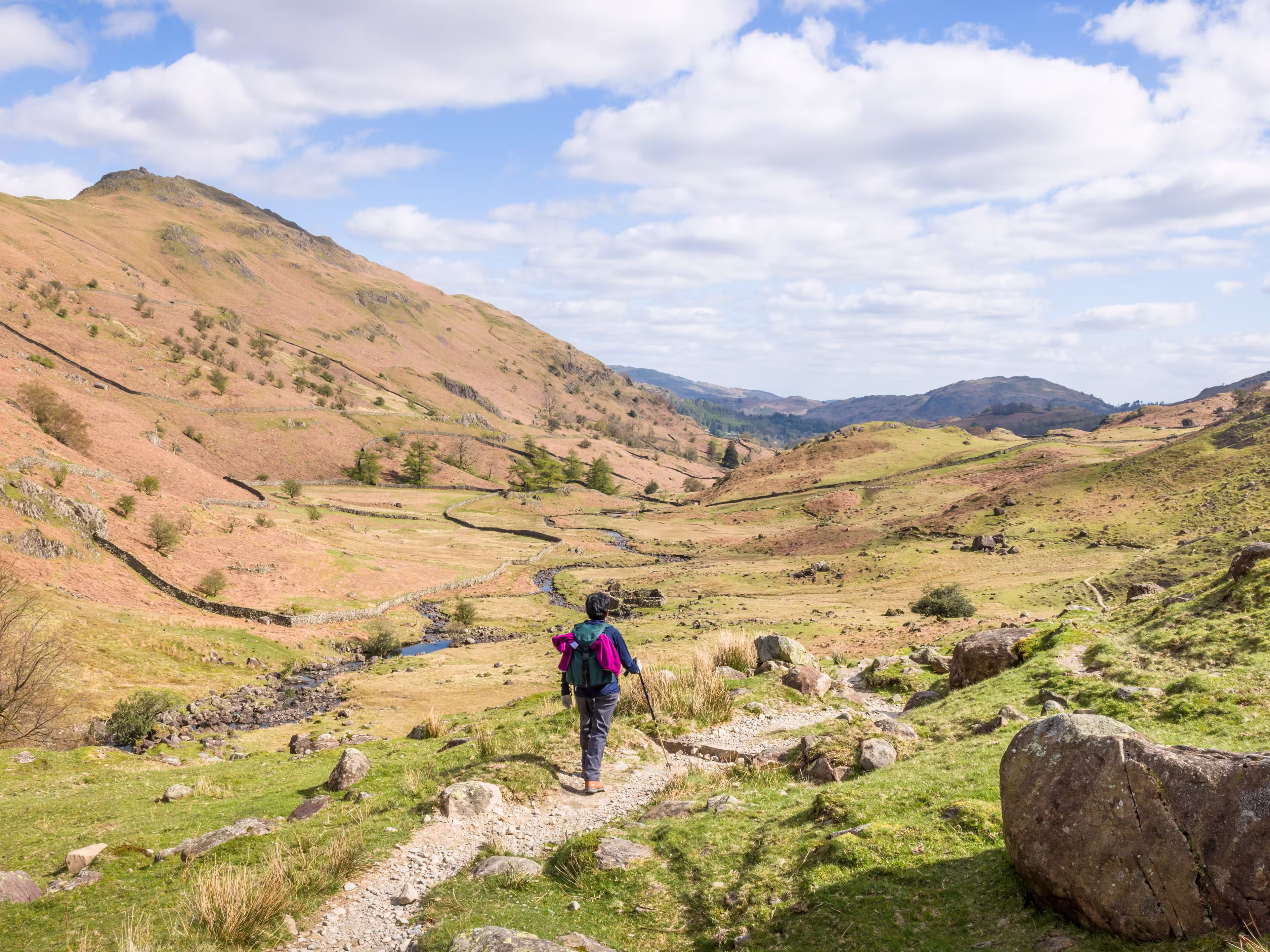Asian Indian woman hiker walking along a footpath in a valley in springtime. Far Easedale Gill, Grasmere, Lake District, UK