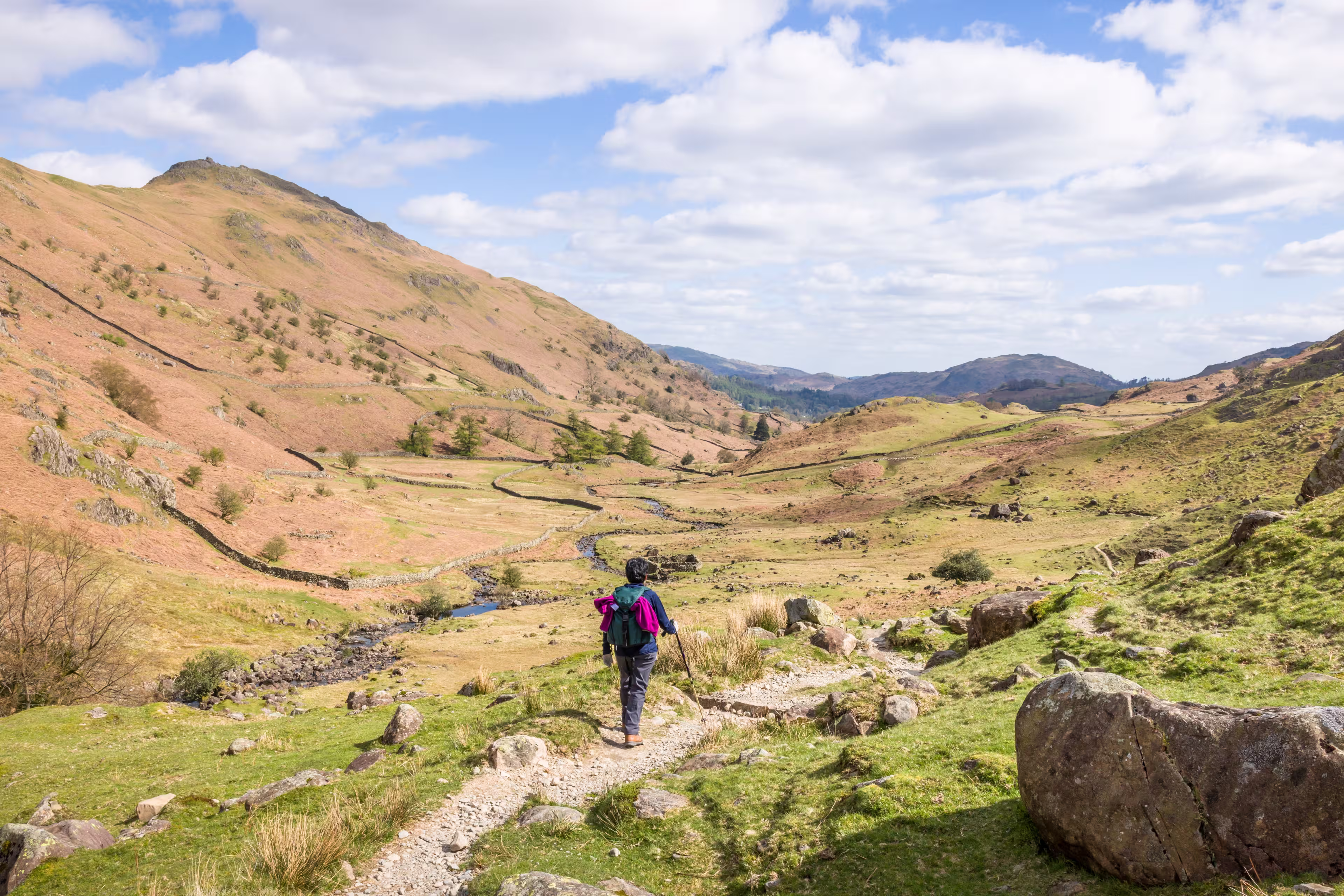 Asian Indian woman hiker walking along a footpath in a valley in springtime. Far Easedale Gill, Grasmere, Lake District, UK
