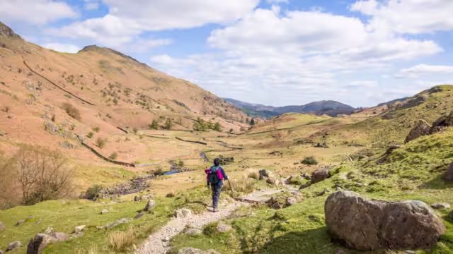 Asian Indian woman hiker walking along a footpath in a valley in springtime. Far Easedale Gill, Grasmere, Lake District, UK