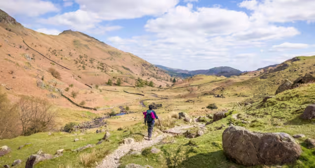 Asian Indian woman hiker walking along a footpath in a valley in springtime. Far Easedale Gill, Grasmere, Lake District, UK