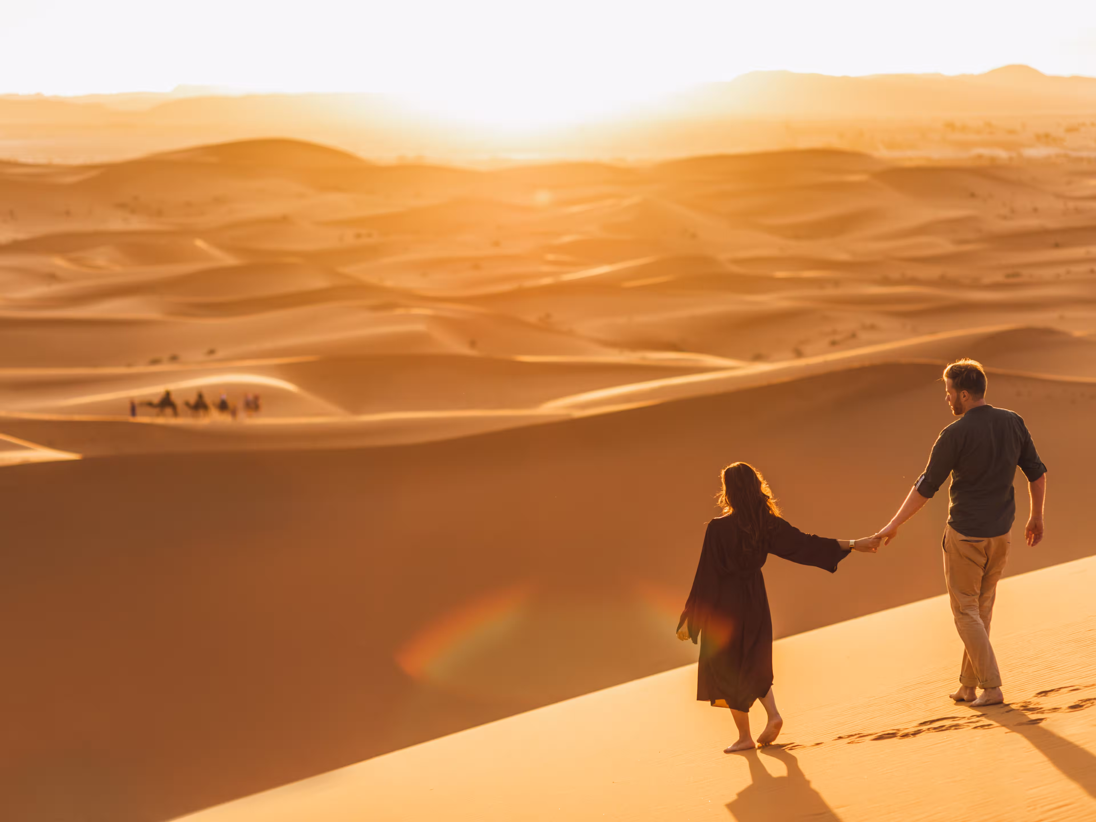 Couple walking in Sahara desert at sunset. View from behind, nature background. Travel, freedom and wanderlust concept.