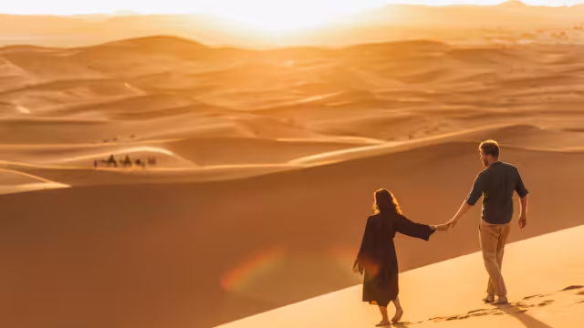 Couple walking in Sahara desert at sunset. View from behind, nature background. Travel, freedom and wanderlust concept.