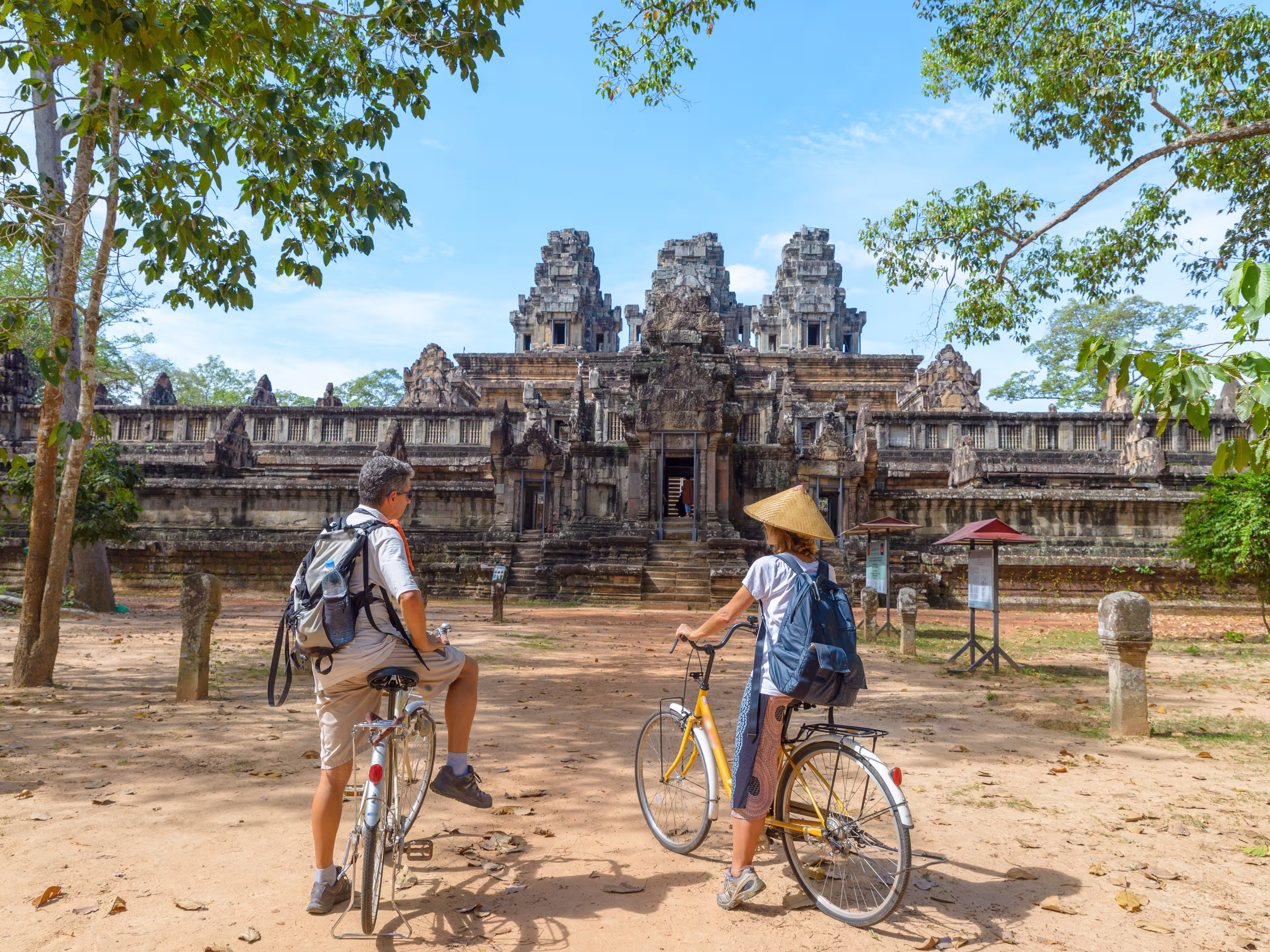 Tourist couple cycling around Angkor temple, Cambodia. Ta Keo building ruins in the jungle. Eco friendly tourism traveling, toned image.