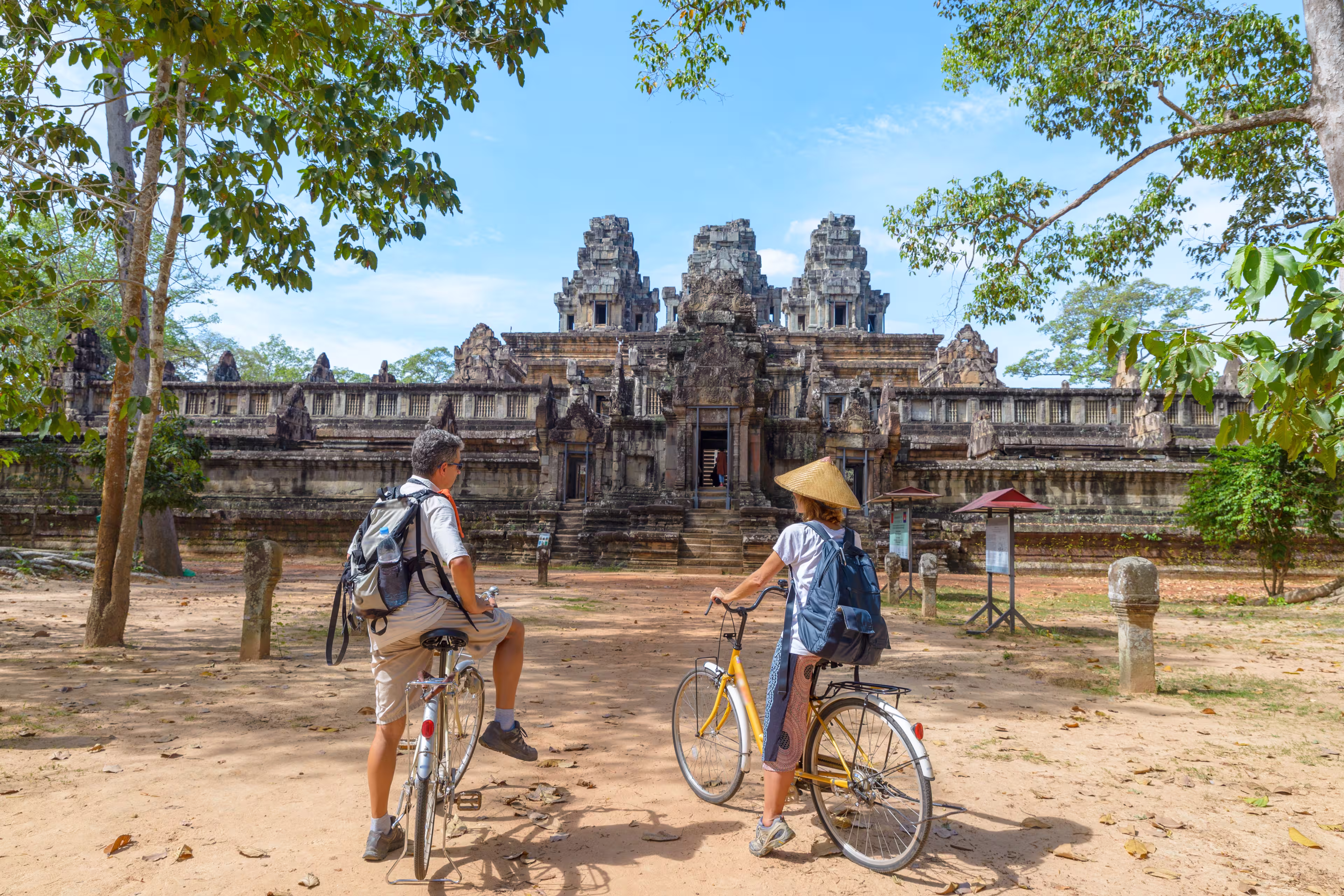 Tourist couple cycling around Angkor temple, Cambodia. Ta Keo building ruins in the jungle. Eco friendly tourism traveling, toned image.