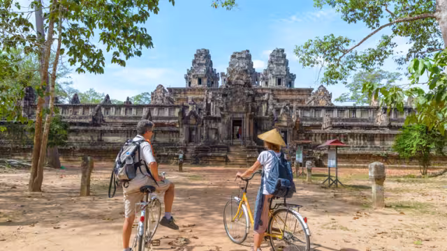 Tourist couple cycling around Angkor temple, Cambodia. Ta Keo building ruins in the jungle. Eco friendly tourism traveling, toned image.