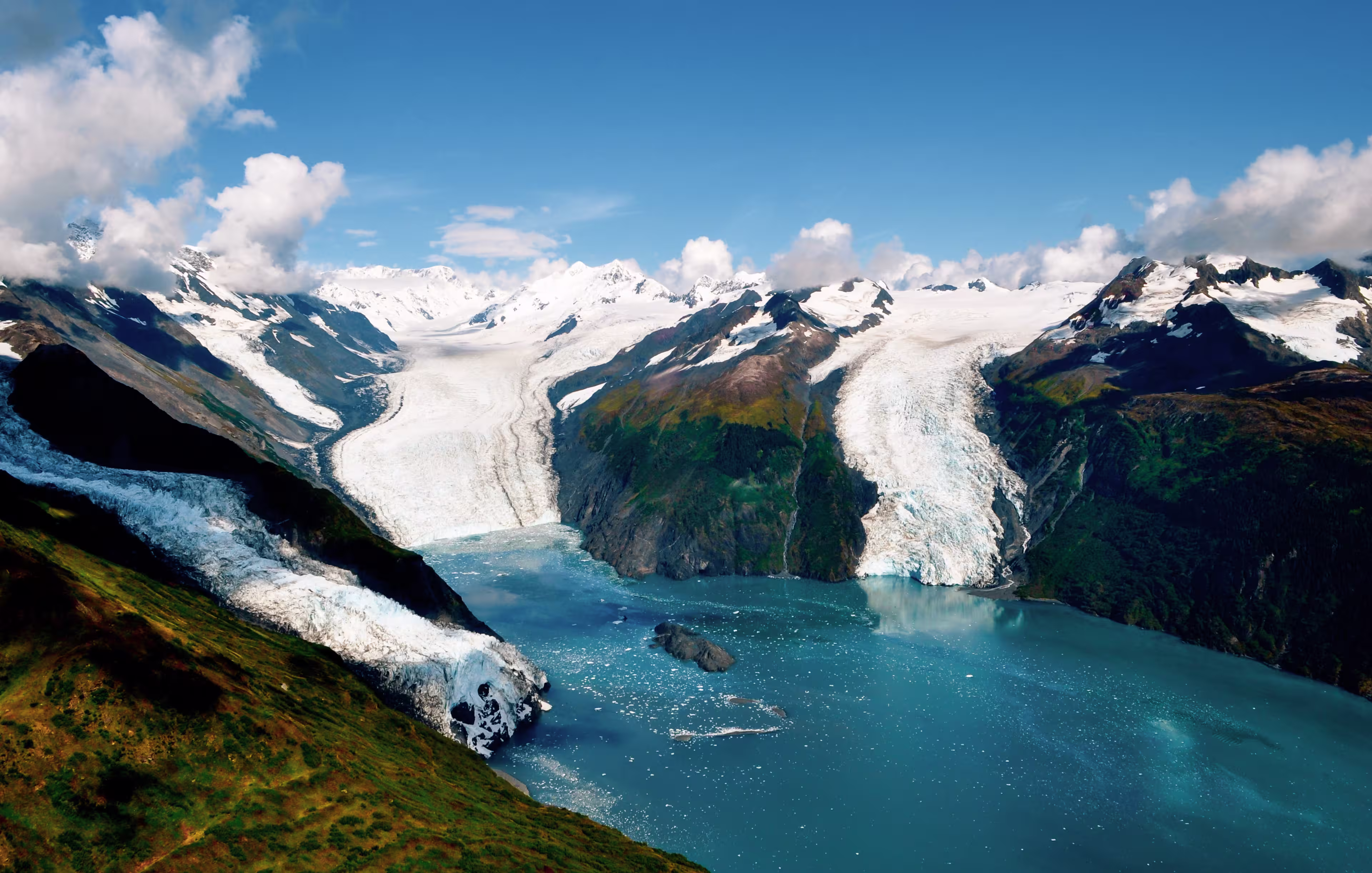 Aerial shot of three majestic glaciers calving into the beautiful azure blue waters of Prince William Sound, Kenai Peninsula. Icebergs float in the water below - Alaska