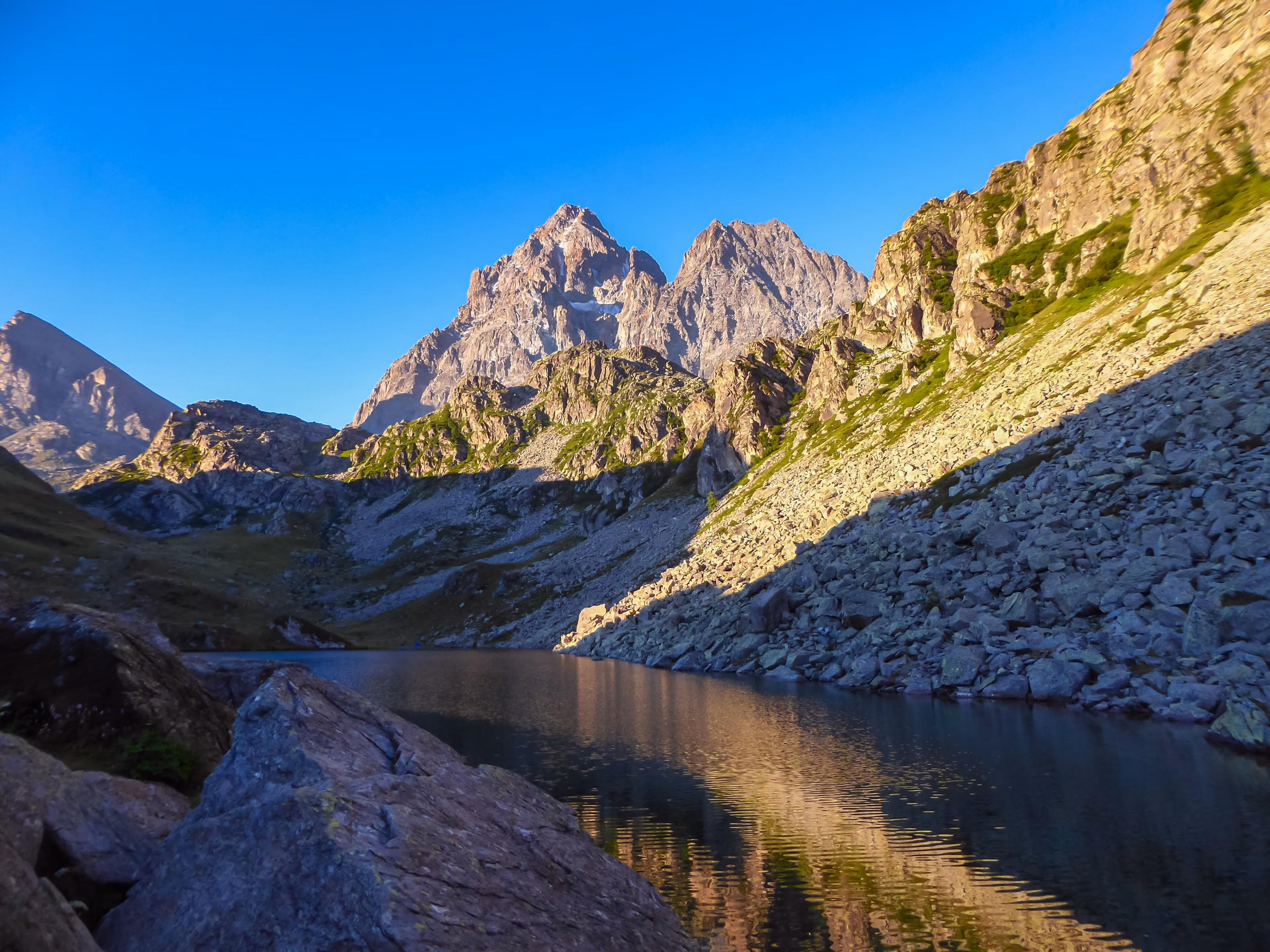 Scenic sunrise view of mountain summit Monte Viso (Monviso) and lake Lago Grande di Viso in the Cottian Alps, Piemonte, Italy, Europe. Rock walls of Stone king are shining in warm red orange colors