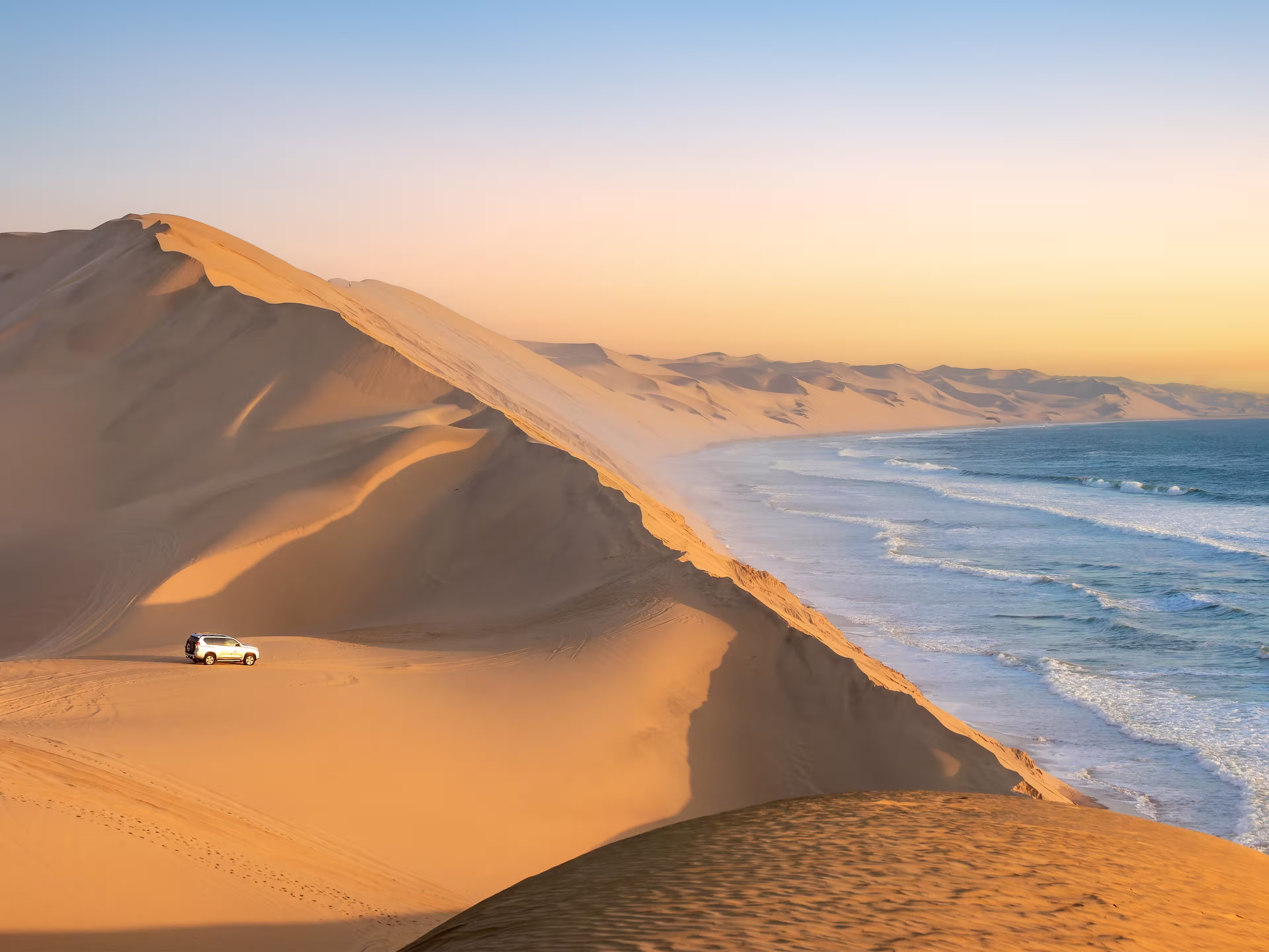 Car in the sand dunes and ocean view in Sandwich Harbour, Namib Naukluft Natural Park landscape in Namibia, Africa