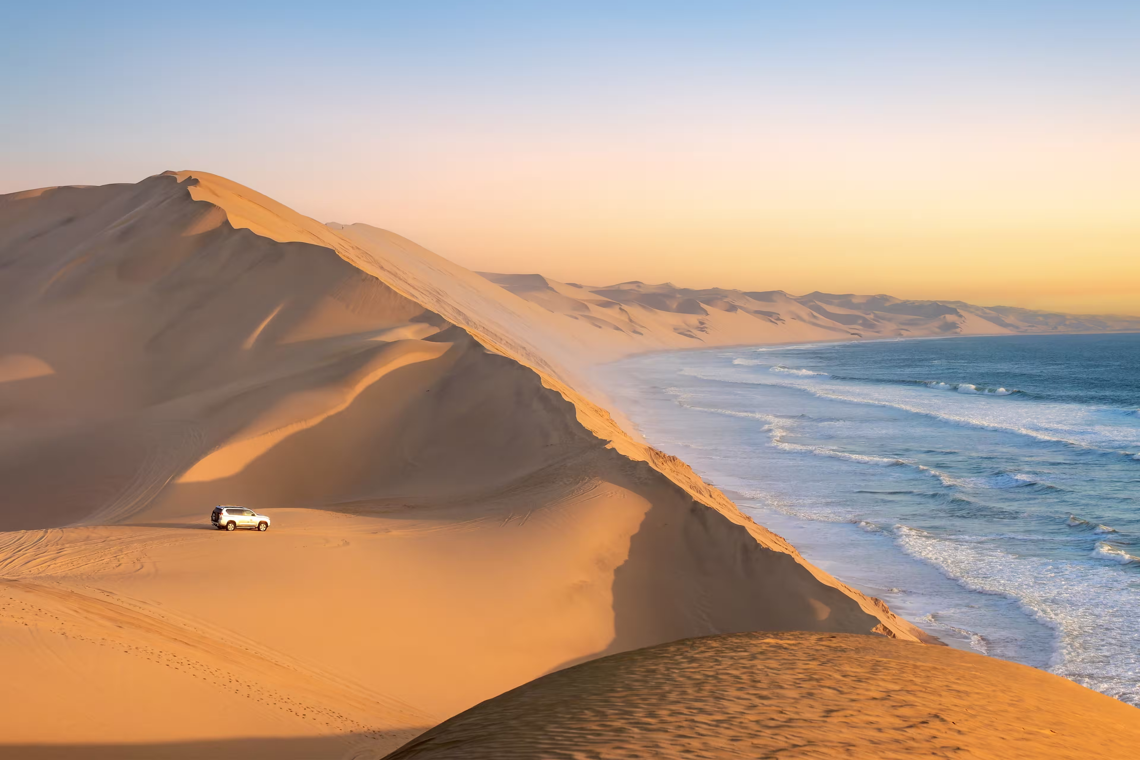 Car in the sand dunes and ocean view in Sandwich Harbour, Namib Naukluft Natural Park landscape in Namibia, Africa