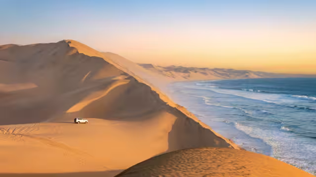 Car in the sand dunes and ocean view in Sandwich Harbour, Namib Naukluft Natural Park landscape in Namibia, Africa