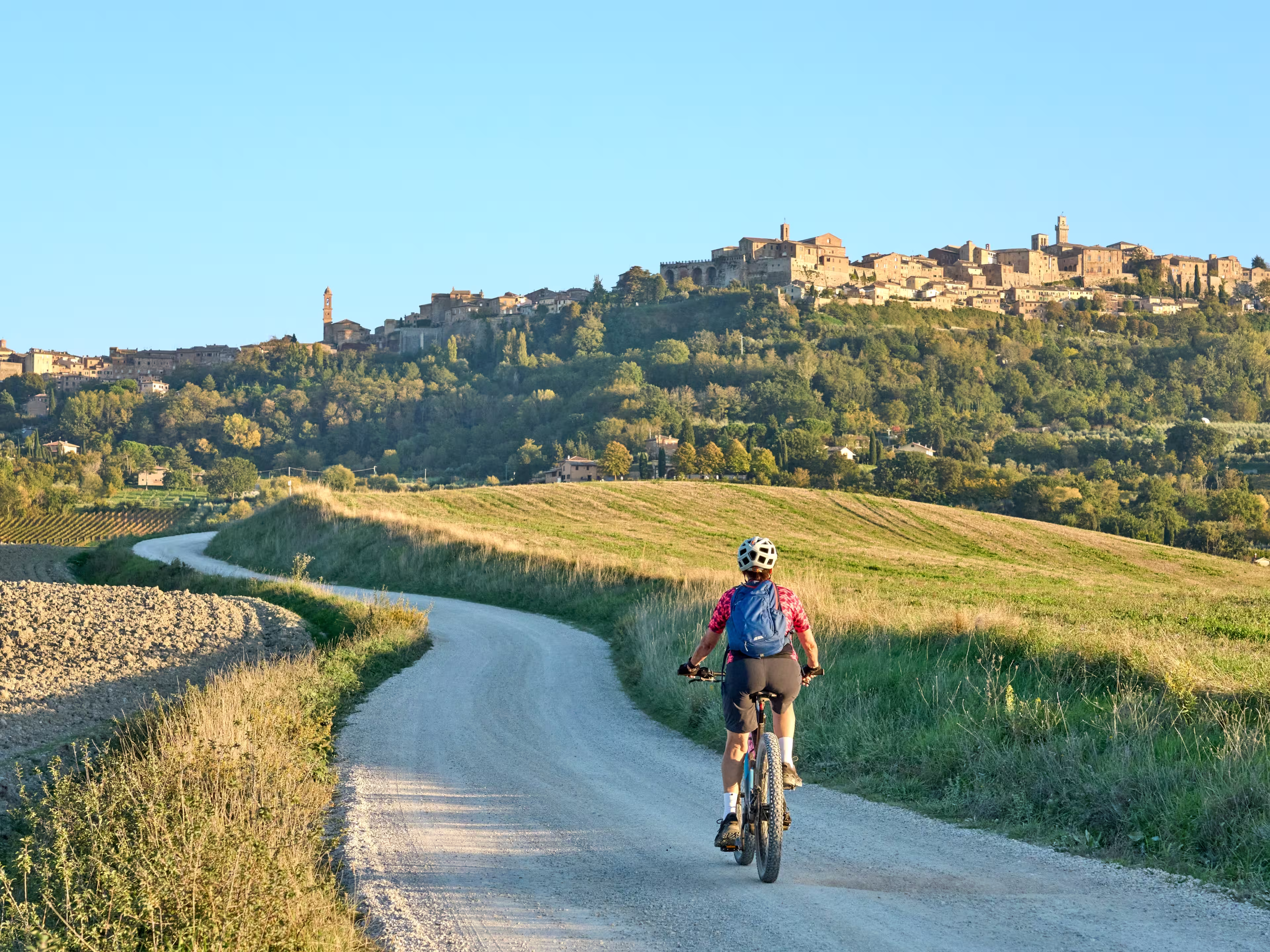 nice senior woman riding her electric mountain bike between olive trees in the Ghianti area with Montepulciano in background, Tuscany , Italy