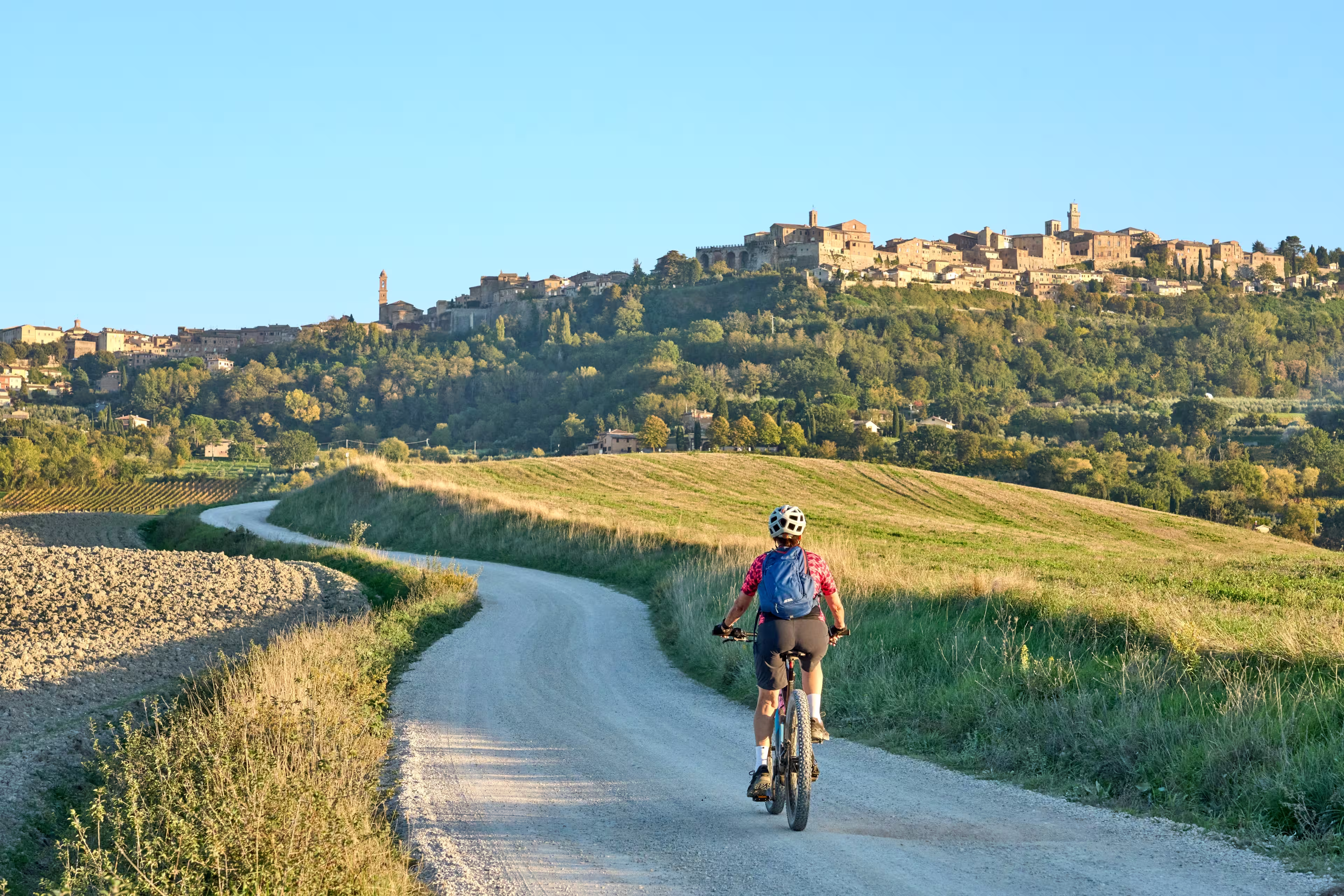 nice senior woman riding her electric mountain bike between olive trees in the Ghianti area with Montepulciano in background, Tuscany , Italy