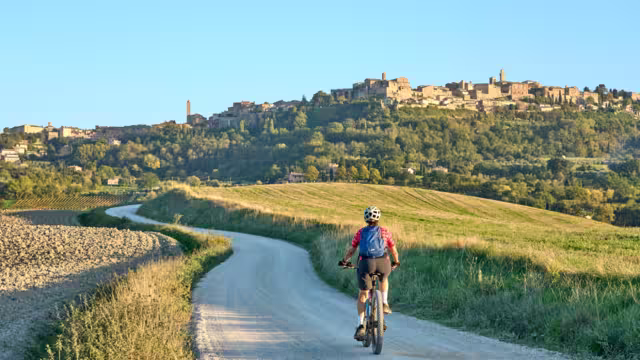 nice senior woman riding her electric mountain bike between olive trees in the Ghianti area with Montepulciano in background, Tuscany , Italy