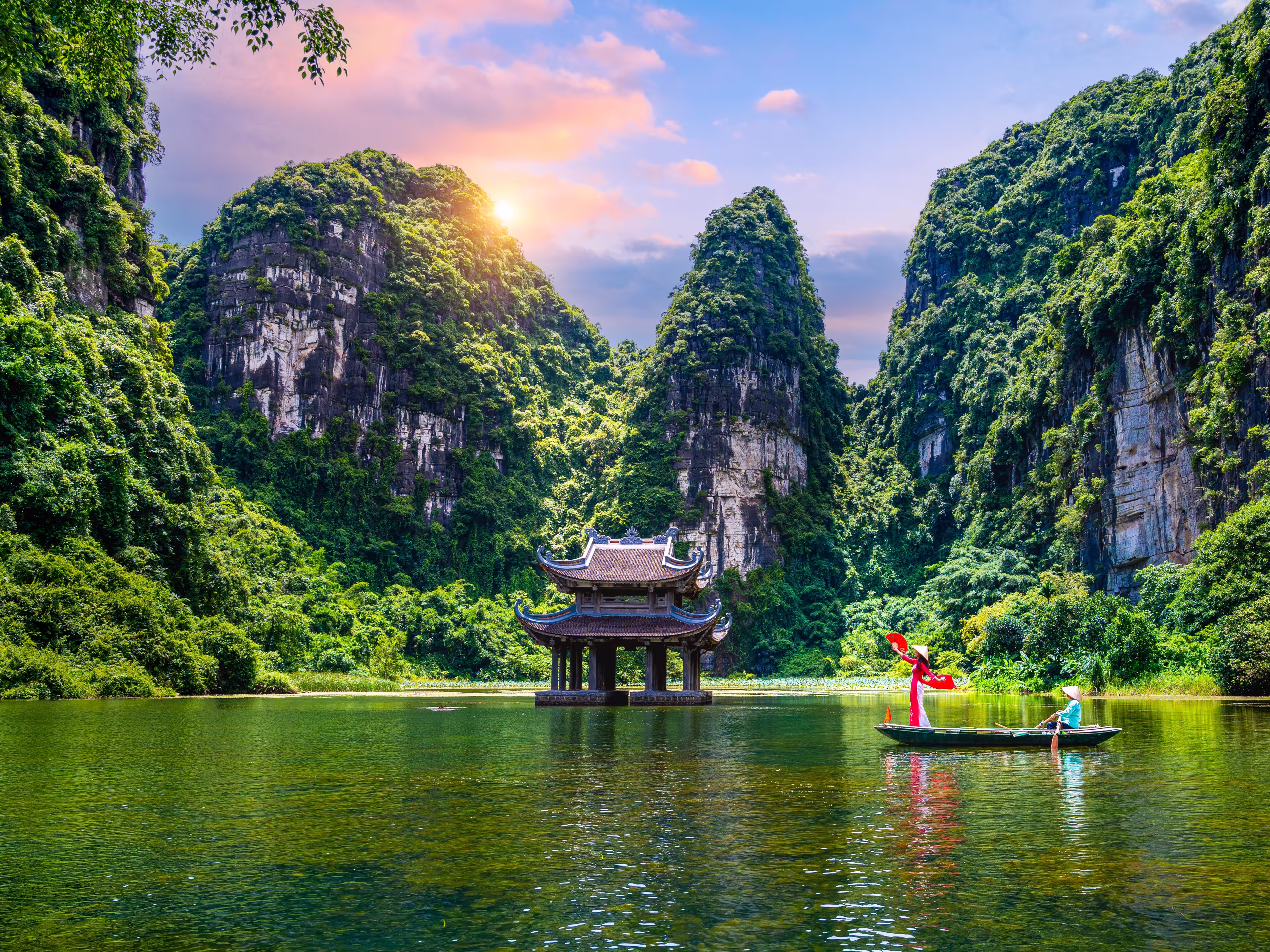 Asian women wearing red traditional Vietnamese cultural clothing on a boat floating in the river flowing through the mountains at Trang An, Vietnam.