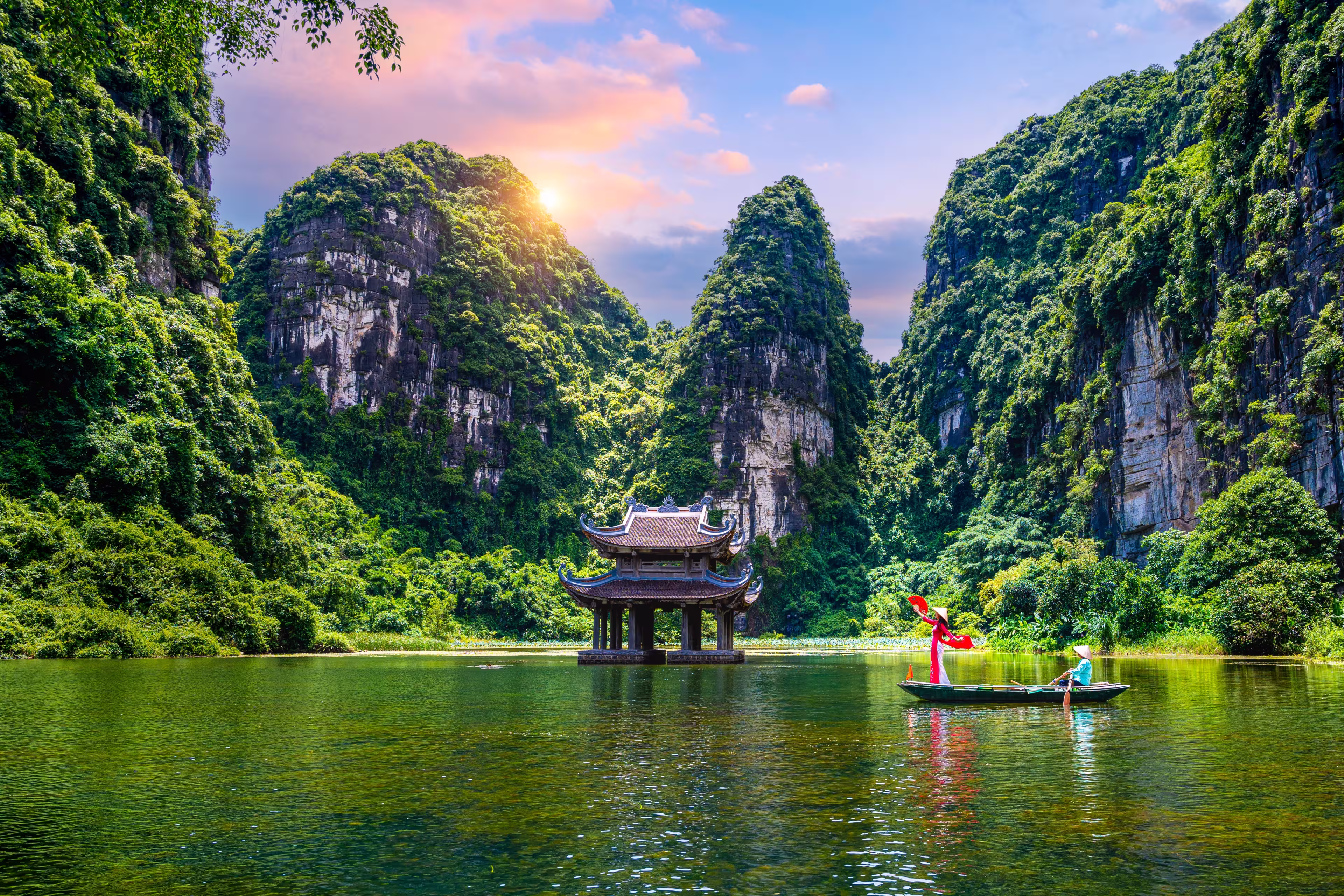 Asian women wearing red traditional Vietnamese cultural clothing on a boat floating in the river flowing through the mountains at Trang An, Vietnam.