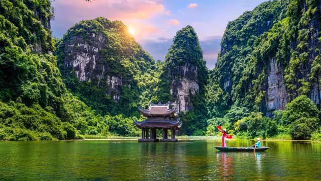 Asian women wearing red traditional Vietnamese cultural clothing on a boat floating in the river flowing through the mountains at Trang An, Vietnam.