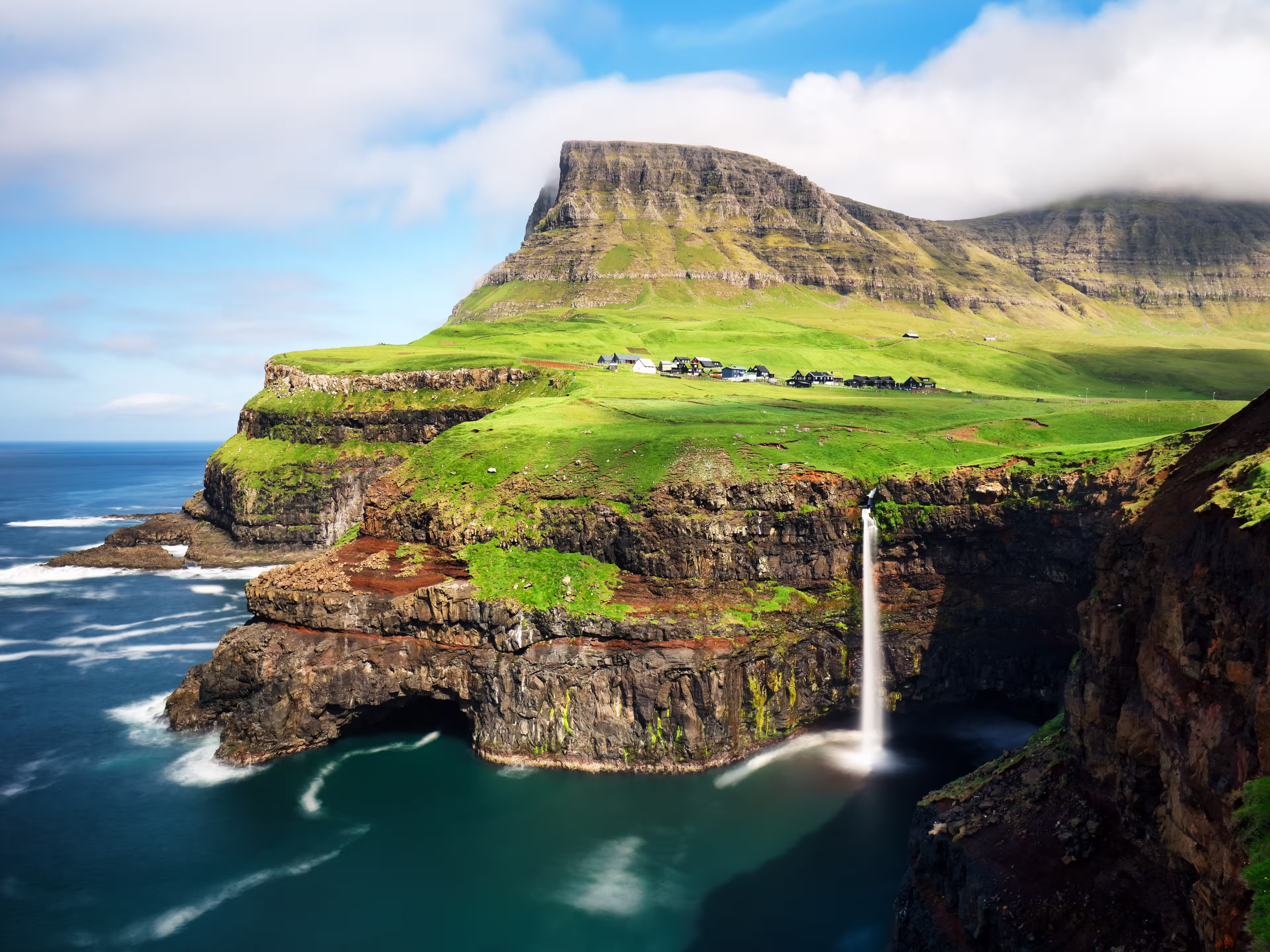 Faroe Islands waterfall Múlafossur near village Gasadalurron the Island Vágar. Green mountain caost landscape.