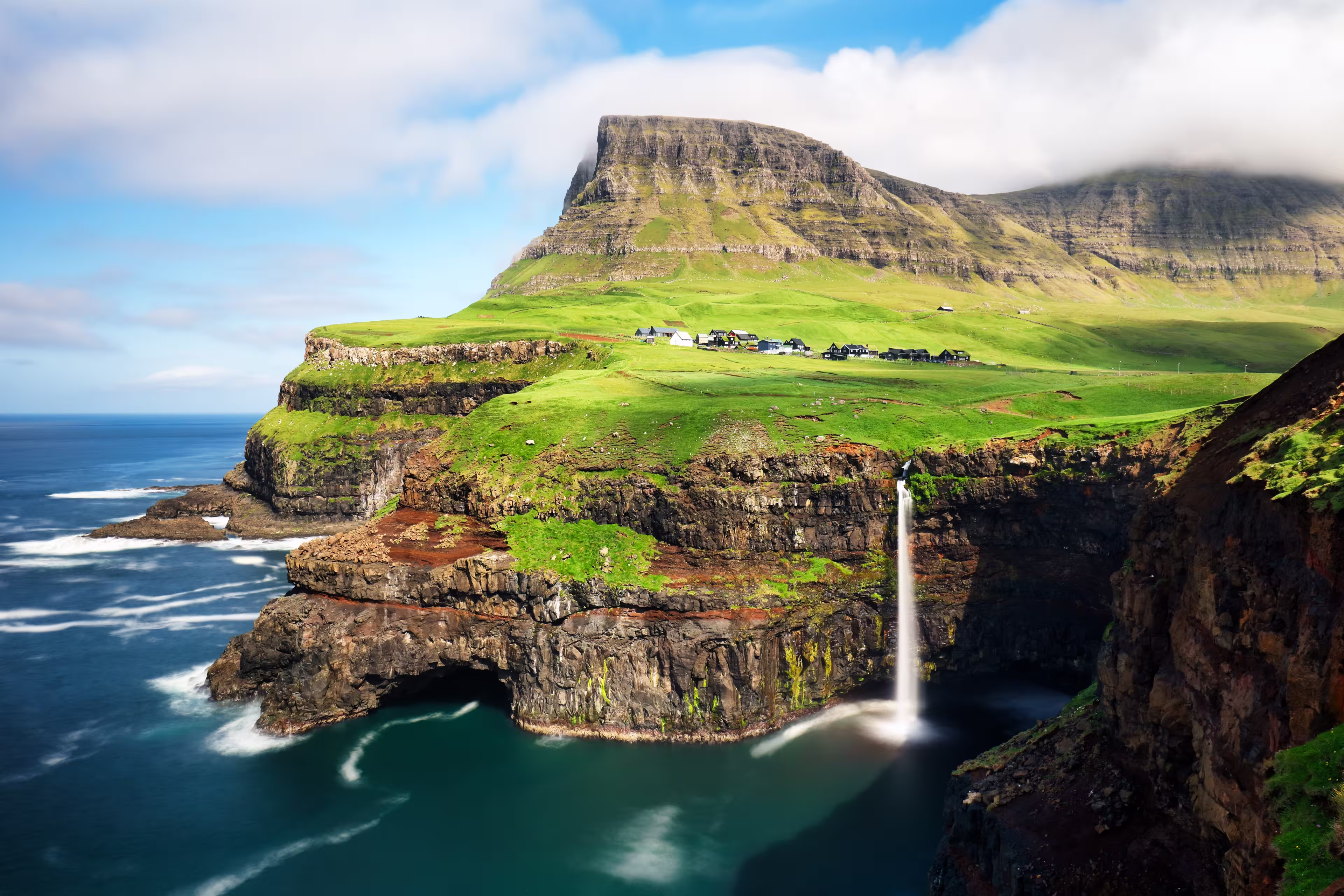 Faroe Islands waterfall Múlafossur near village Gasadalurron the Island Vágar. Green mountain caost landscape.
