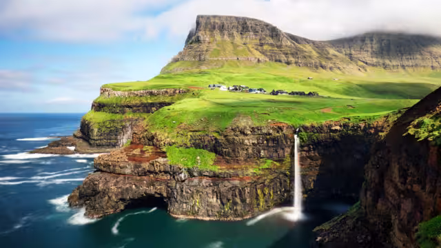 Faroe Islands waterfall Múlafossur near village Gasadalurron the Island Vágar. Green mountain caost landscape.