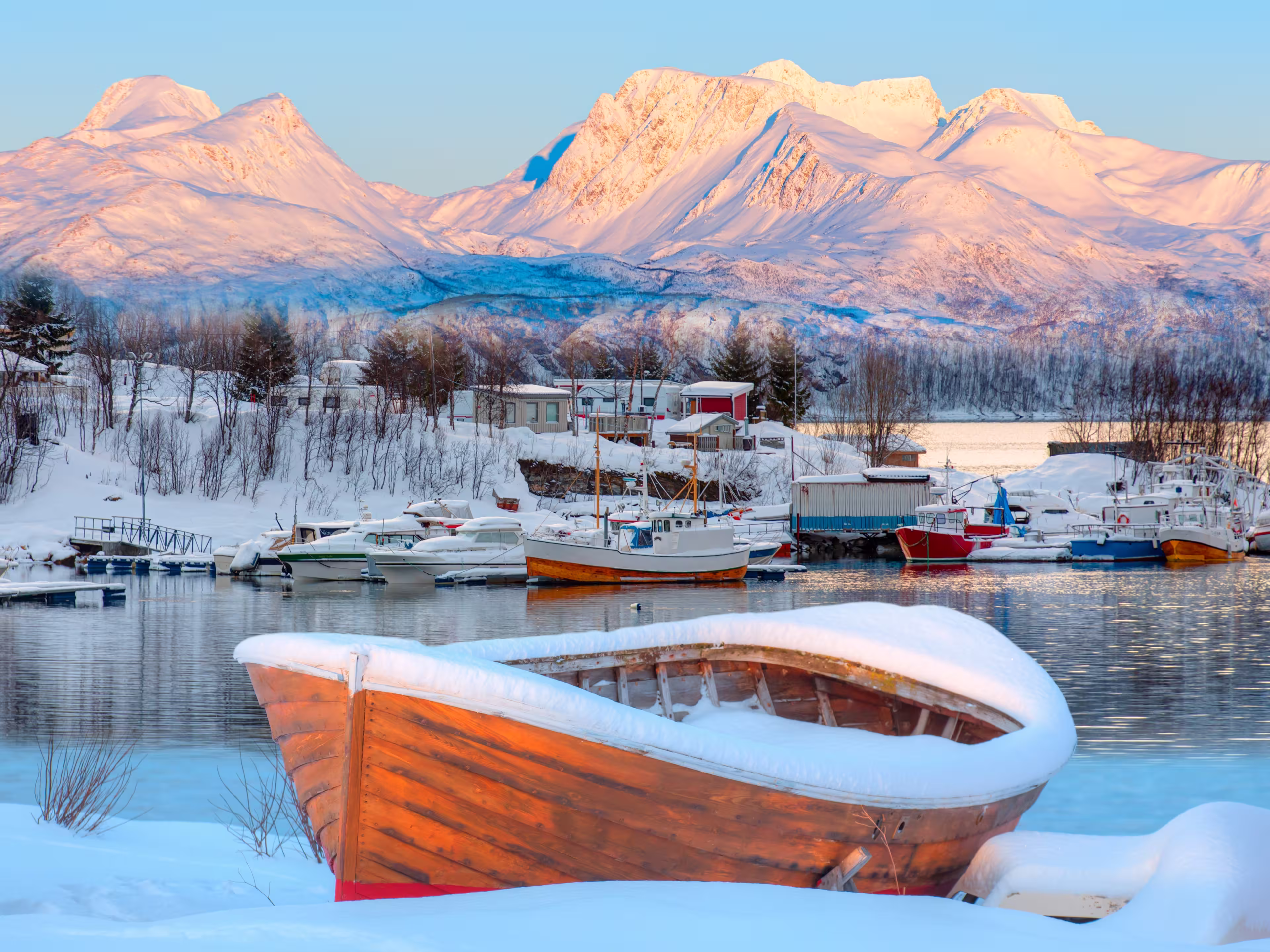 Fisher shelter in winter with fishboat at sunset in the background snowy mountains and Norwegian fjords - Tromso, Norway