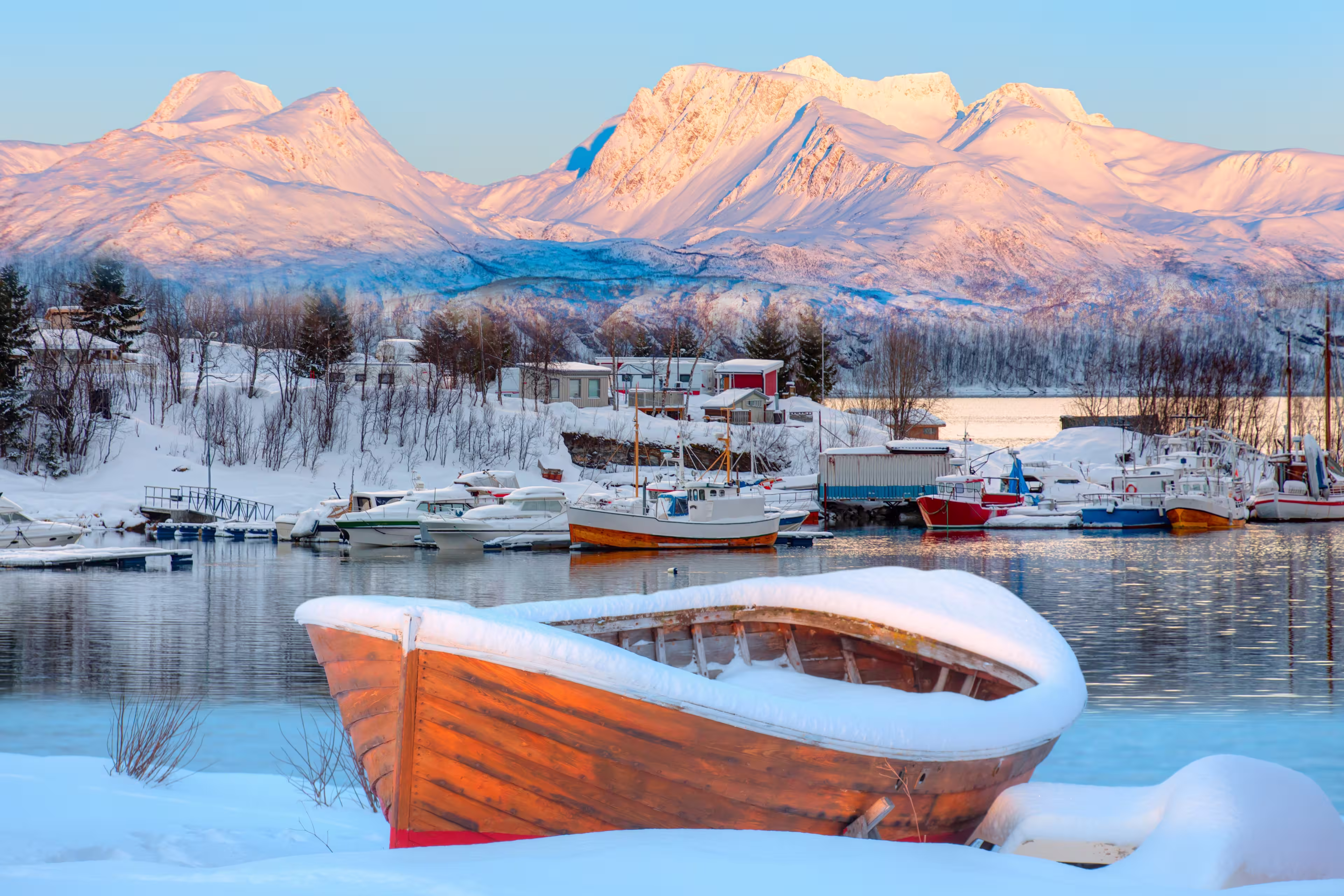 Fisher shelter in winter with fishboat at sunset in the background snowy mountains and Norwegian fjords - Tromso, Norway