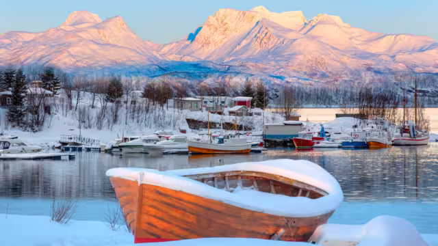 Fisher shelter in winter with fishboat at sunset in the background snowy mountains and Norwegian fjords - Tromso, Norway
