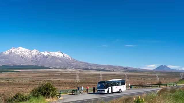 Travellers' tour bus pulled over on side of road so travellers can enjoy the view of Mount Tongariro, New Zealand