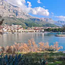 Autumn view of Makarska set between the calm Adriatic Sea and the rugged Biokovo mountains, where coastal architecture meets dramatic limestone slopes under soft seasonal light.