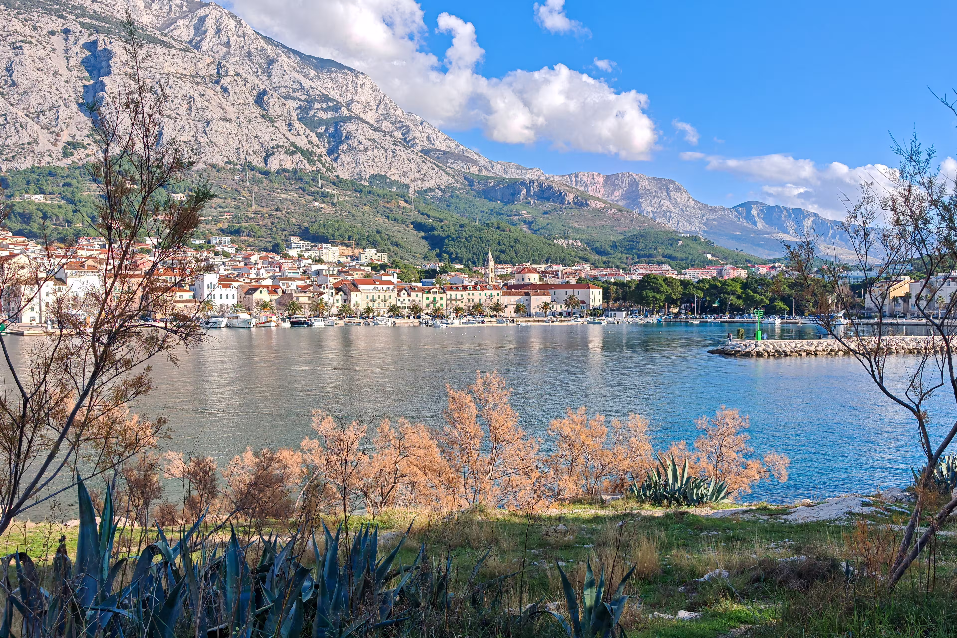 Autumn view of Makarska set between the calm Adriatic Sea and the rugged Biokovo mountains, where coastal architecture meets dramatic limestone slopes under soft seasonal light.