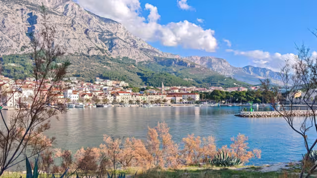 Autumn view of Makarska set between the calm Adriatic Sea and the rugged Biokovo mountains, where coastal architecture meets dramatic limestone slopes under soft seasonal light.