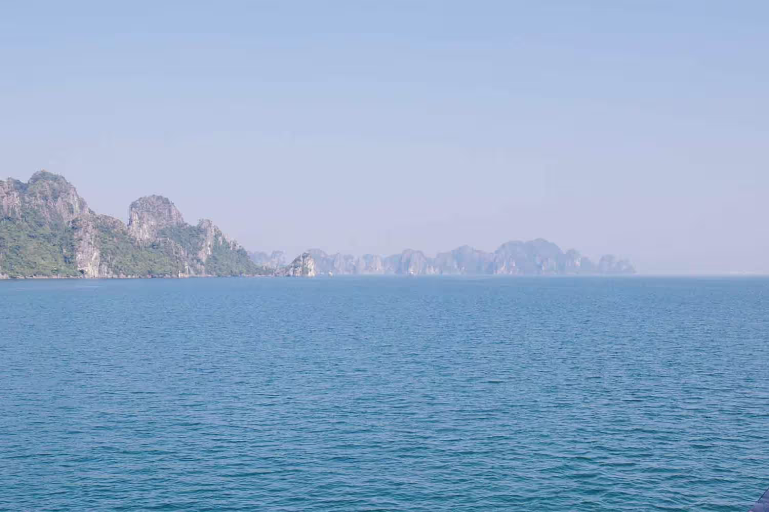 Passengers on board boat look out at the mountainous islands of Halong bay