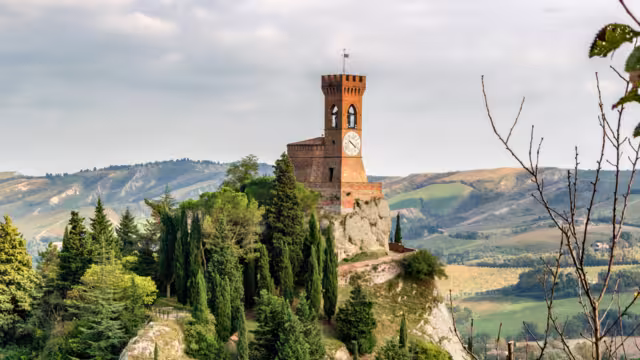 The medieval clock tower surrounded by cypress and other trees, viewed from the Rock of Brisighella in Emilia Romagna, Italy.