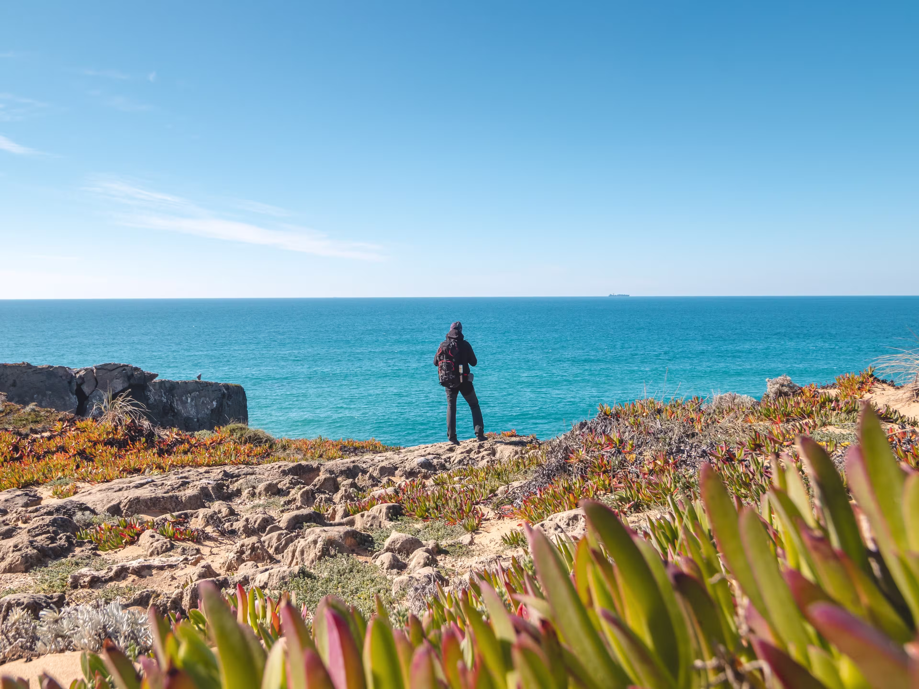 Passionate young backpacker tracks rocky cliffs on the Atlantic coast near Vila Nova de Milfontes, Odemira, Portugal. In the footsteps of Rota Vicentina. Fisherman trail.