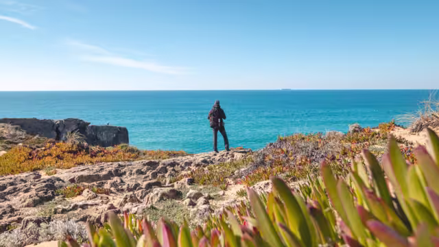 Passionate young backpacker tracks rocky cliffs on the Atlantic coast near Vila Nova de Milfontes, Odemira, Portugal. In the footsteps of Rota Vicentina. Fisherman trail.