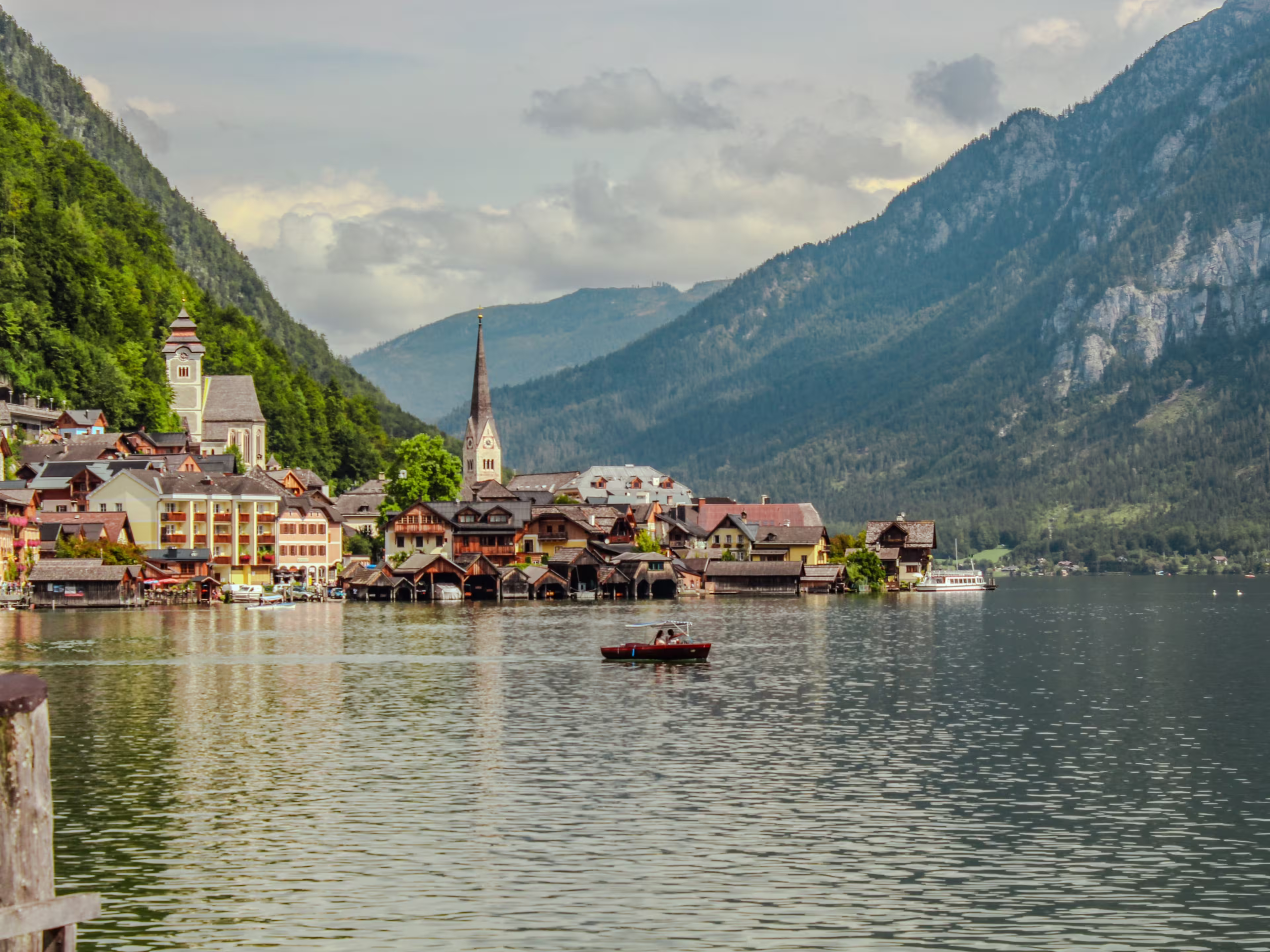 Pristine alpine lake Hallstatt with mirror-like water reflection, surrounded by Dachstein mountains in Austria. Charming traditional houses and iconic Lutheran church on shore.
