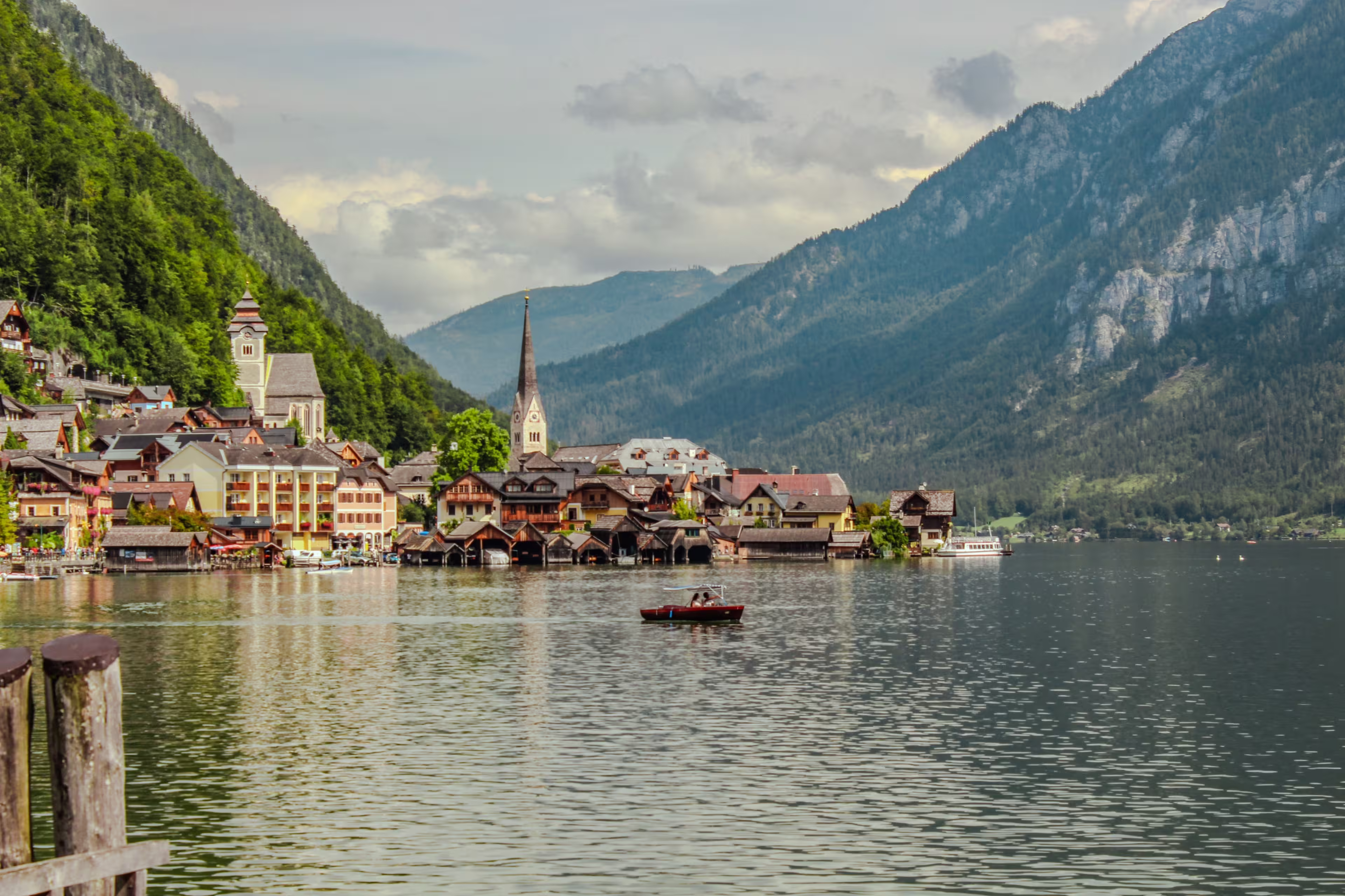 Pristine alpine lake Hallstatt with mirror-like water reflection, surrounded by Dachstein mountains in Austria. Charming traditional houses and iconic Lutheran church on shore.