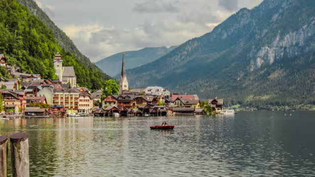 Pristine alpine lake Hallstatt with mirror-like water reflection, surrounded by Dachstein mountains in Austria. Charming traditional houses and iconic Lutheran church on shore.