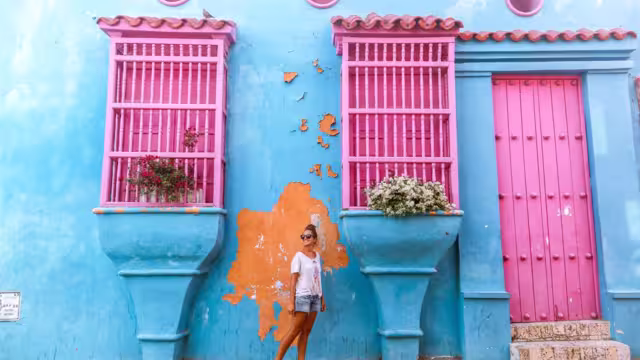 Traveller smiling in front of bright blue and pink building in Cartagena, Colombia