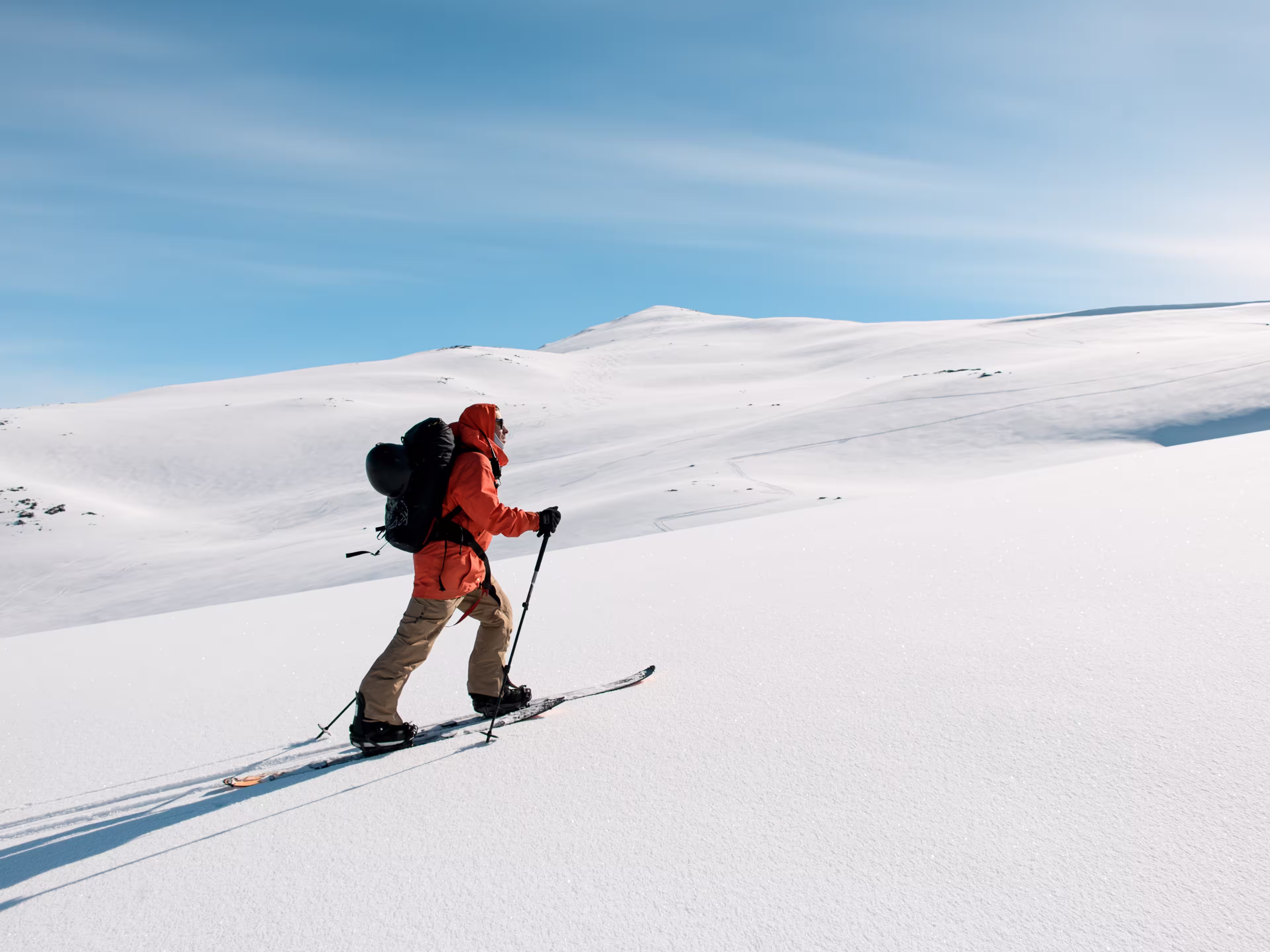 Side view of skier in orange jacket moving up gentle snowy mountain slope on skis