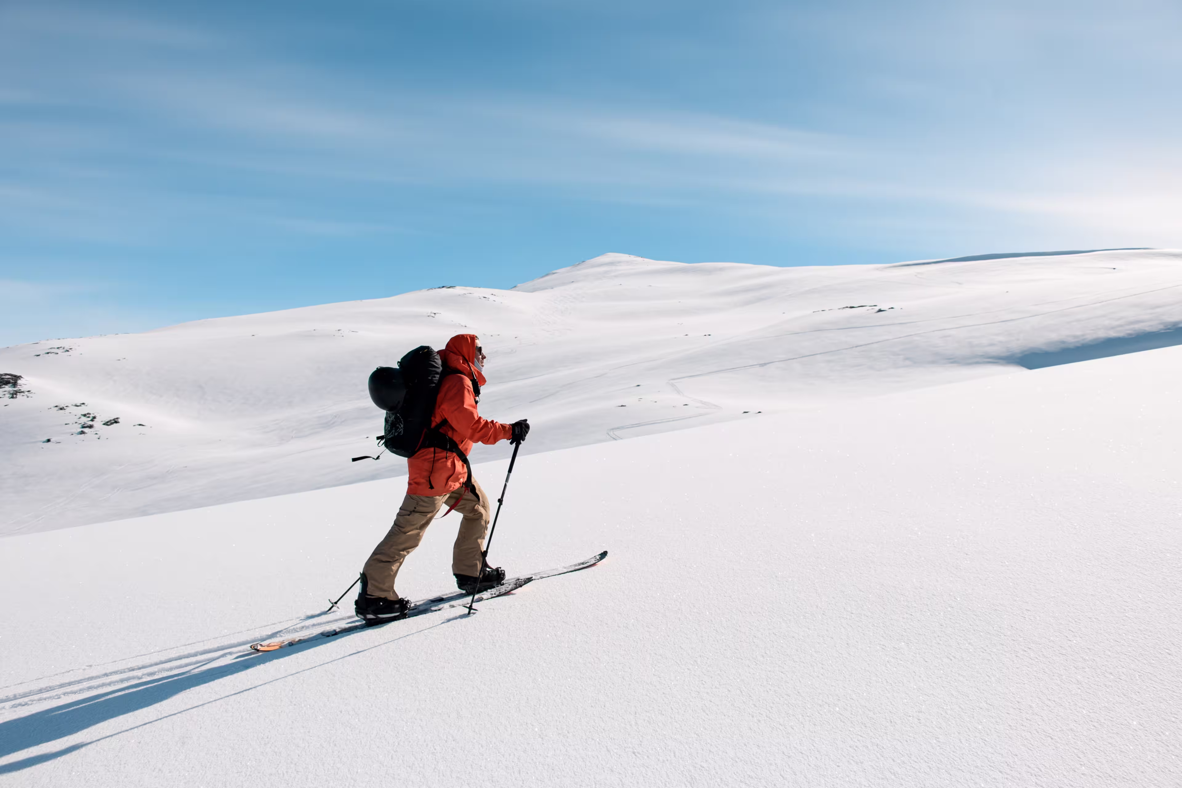 Side view of skier in orange jacket moving up gentle snowy mountain slope on skis