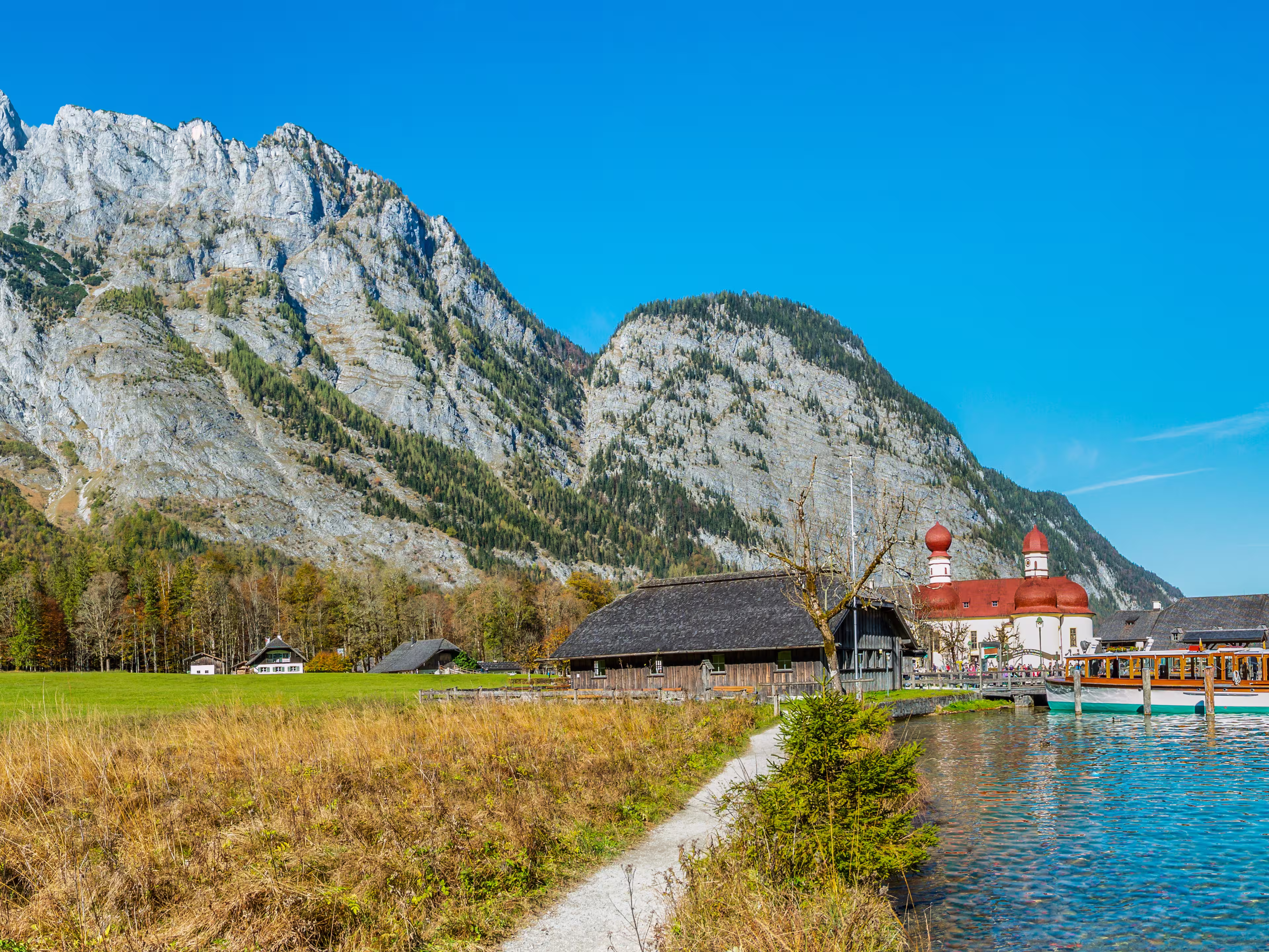 Panorama image of the Koenigssee with the chapel of st bartholomew and a tourist boat. In the background the illuminated mountain formation of Watzmann in bavaria, Germany