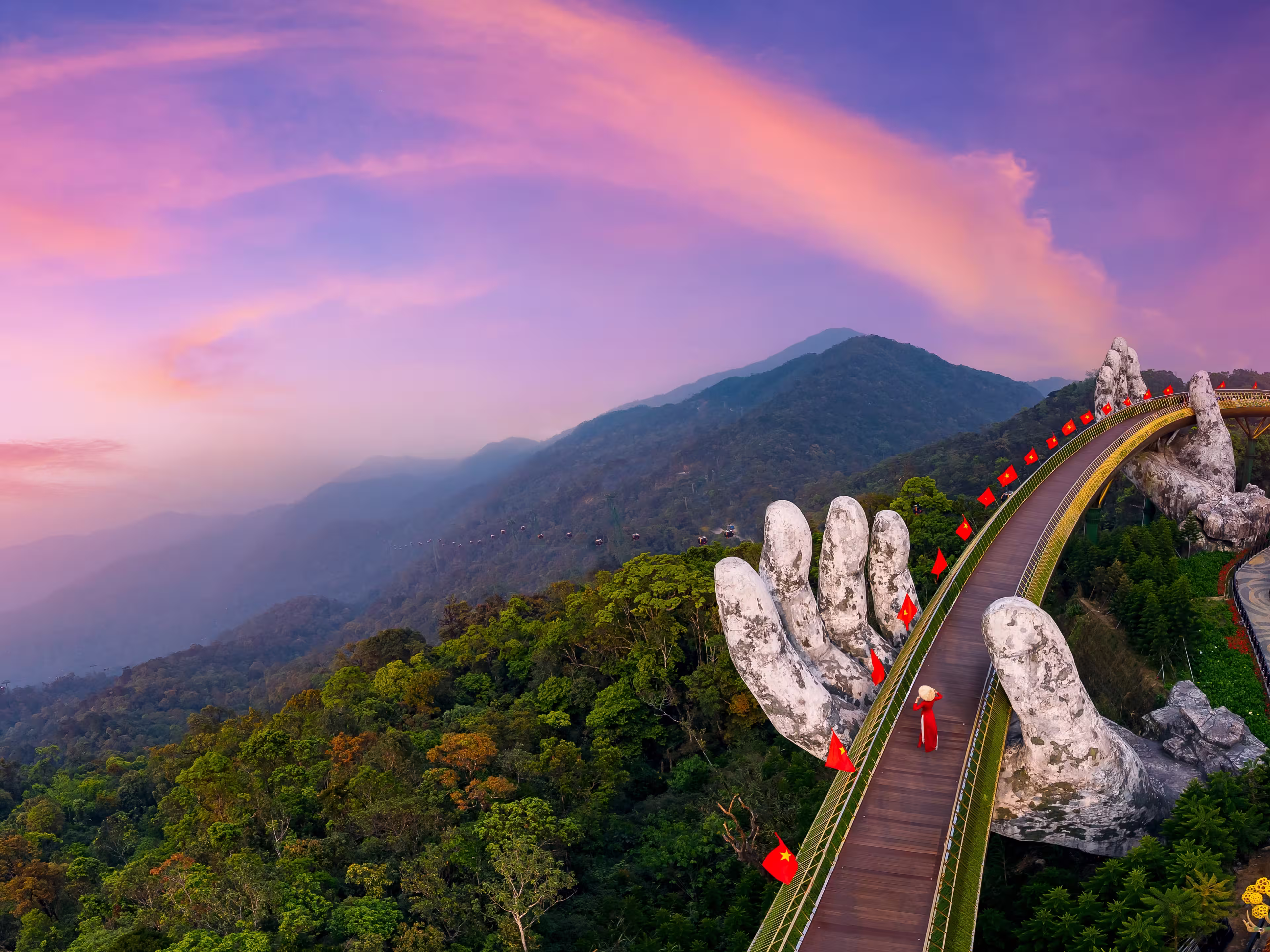 Aerial view woman tourist with traditional dress on Golden bridge at ba na hills in Da nang, Vietnam at sunset.