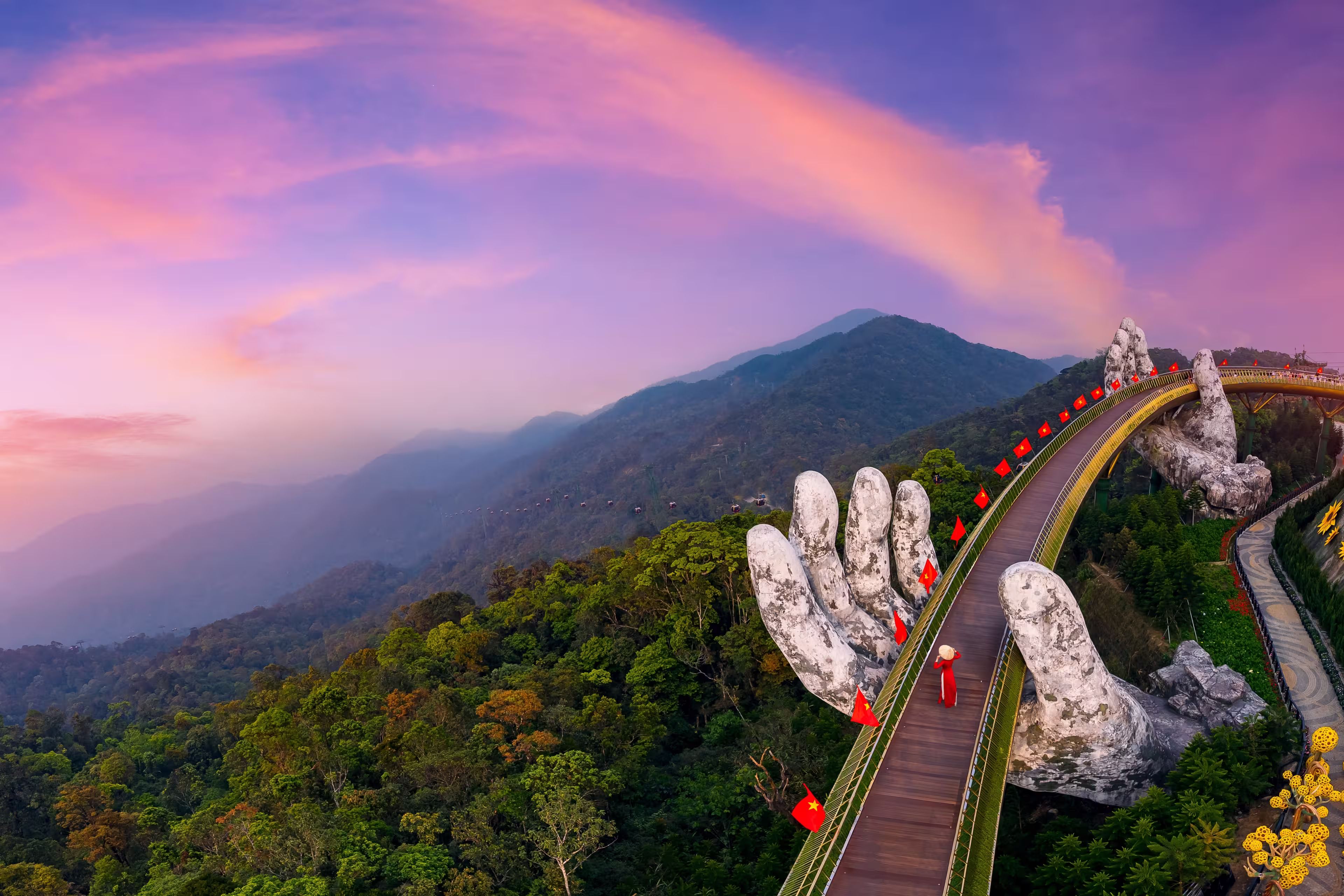 Aerial view woman tourist with traditional dress on Golden bridge at ba na hills in Da nang, Vietnam at sunset.