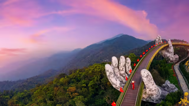 Aerial view woman tourist with traditional dress on Golden bridge at ba na hills in Da nang, Vietnam at sunset.
