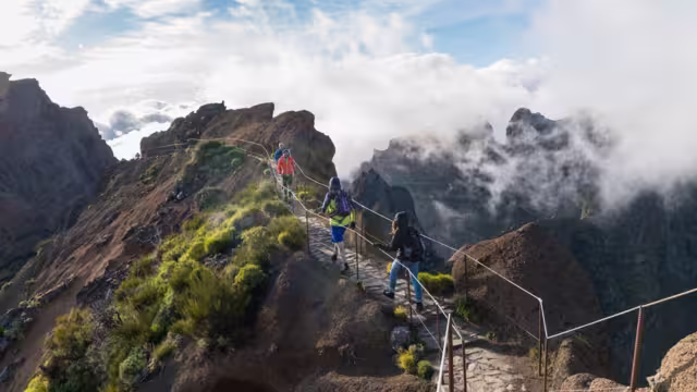 Travellers hike a narrow mountaintop path on the way to Pico do Ruivo in the sunlight of Madeira, Portugal